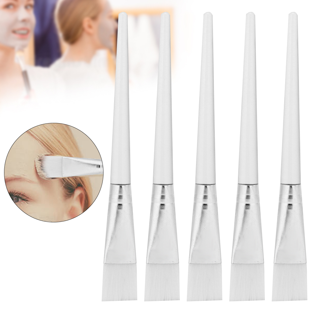 Fünf weiße Kosmetikpinsel mit silbernem Sockel, vor zwei verschwommenen Frauen, die Gesichtsmasken auftragen. Ein Pinsel trägt Maske auf.