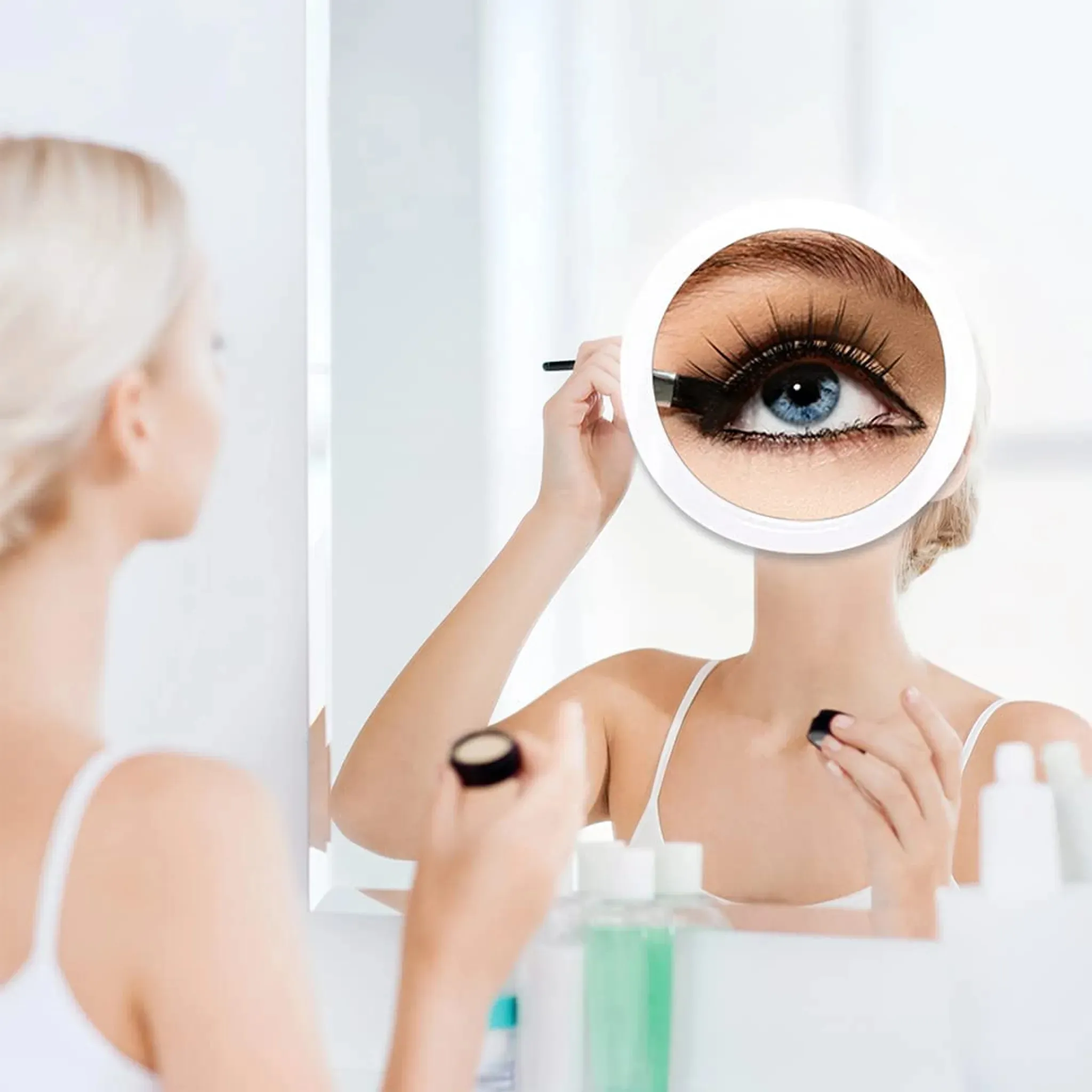 Frau, die sich im Spiegel Eyeliner aufträgt. Ein vergrößertes Auge ist im Spiegel zu sehen. Sie trägt ein weißes Oberteil.