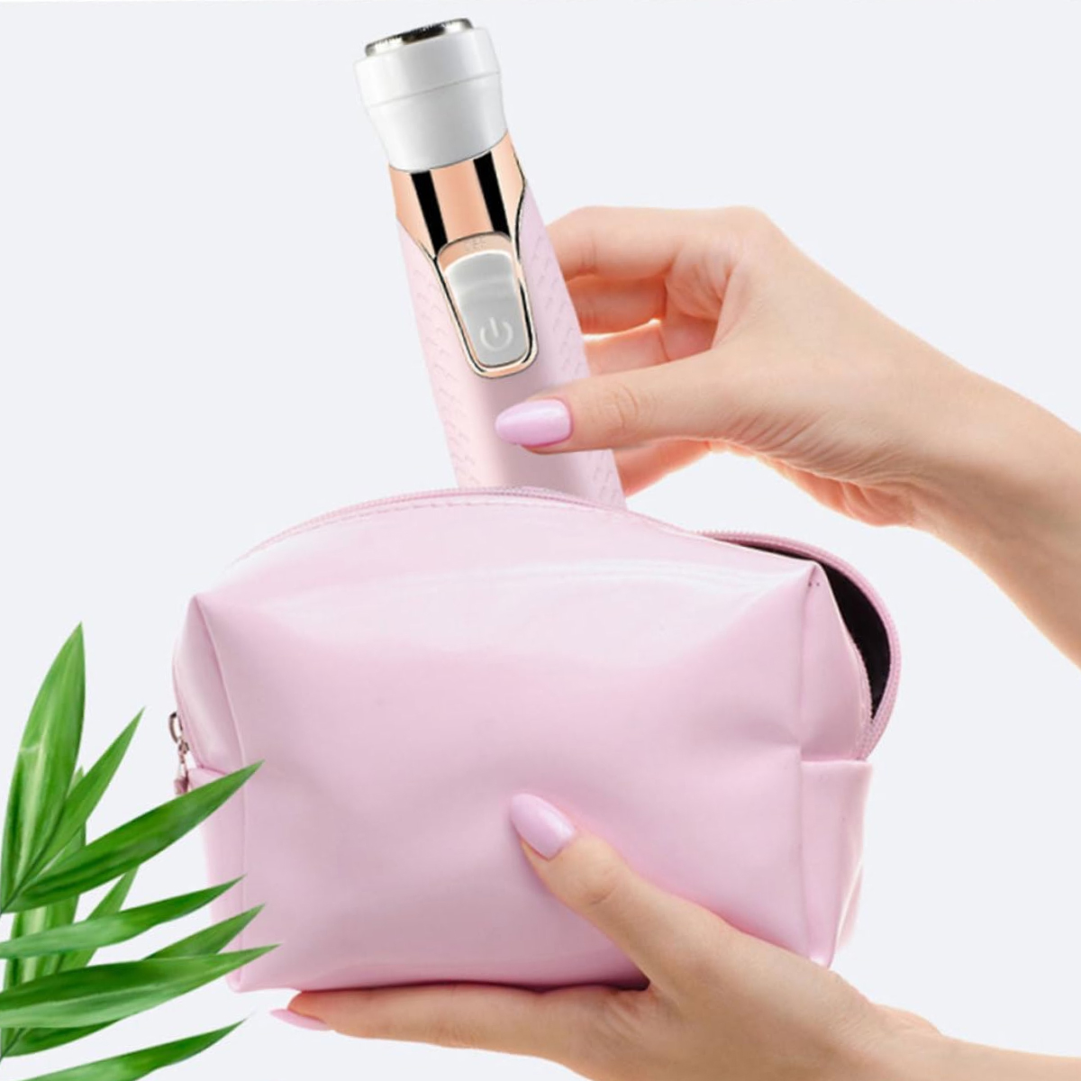 Ein pinkfarbener Elektrorasierer wird von Frauenhänden in eine pinkfarbene Kosmetiktasche gelegt. Grüne Blätter sind im Hintergrund.