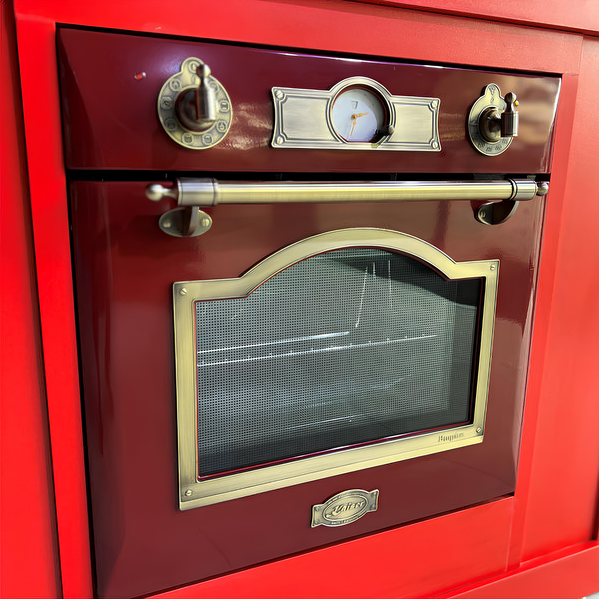 Roter Spielzeugofen mit Messingdetails. Knöpfe, Griff und Ofenfenster sind sichtbar. Der Ofen steht auf einem roten Schrank.