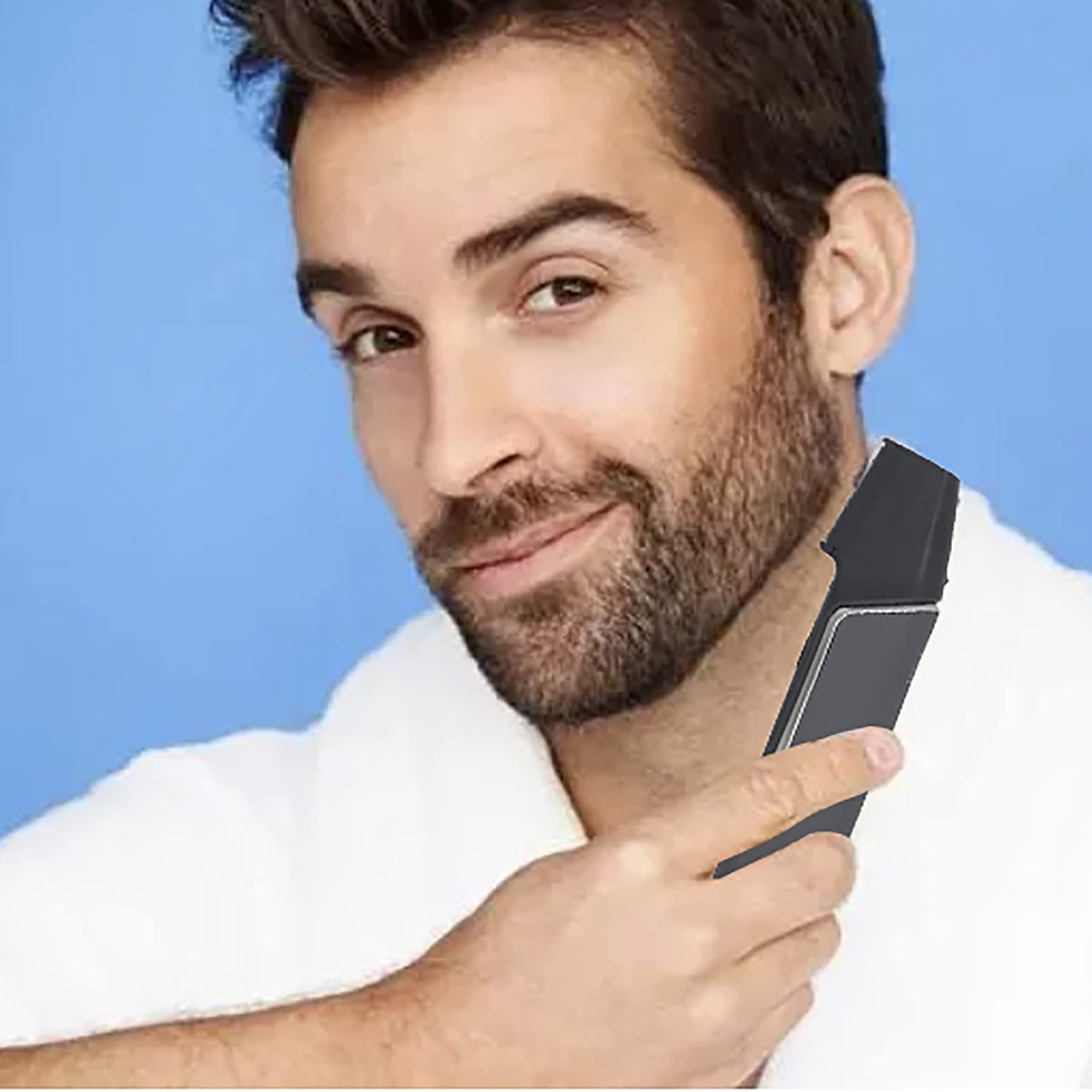 Ein Mann im weißen Bademantel rasiert seinen Bart mit einem schwarzen Trimmer vor blauem Hintergrund, lächelnd.