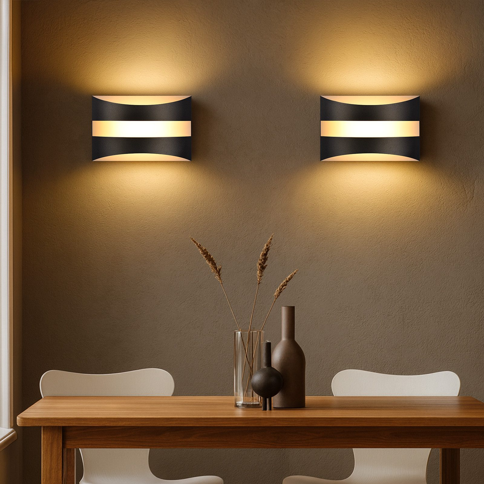 Due lampade da parete a strisce bianche e nere sopra un tavolo di legno. Un vaso con piante e sedie sono visibili.
