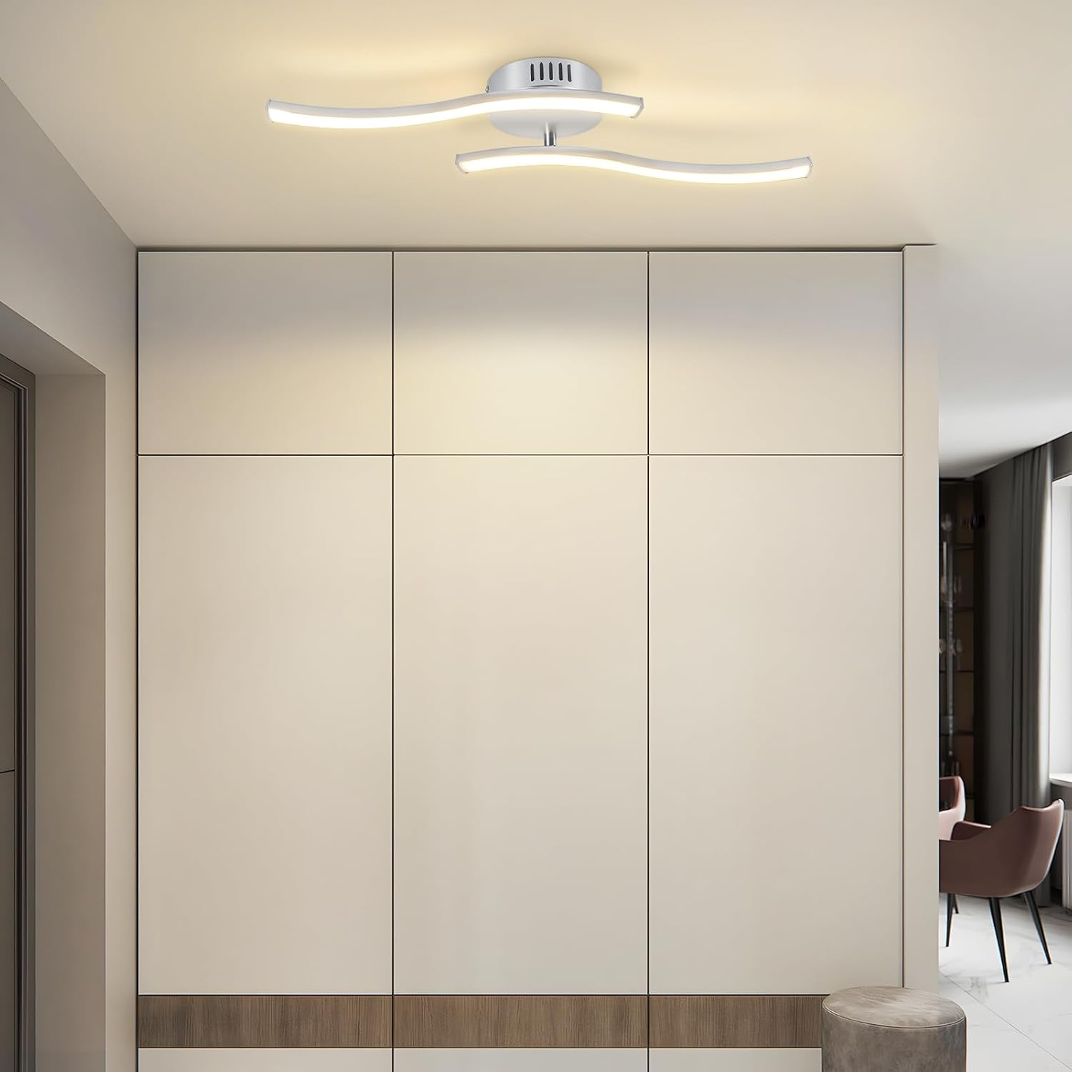 Una moderna lampada da soffitto bianca, un grande armadio bianco e uno sgabello rotondo sono in una stanza. Sullo sfondo si vede una sedia.