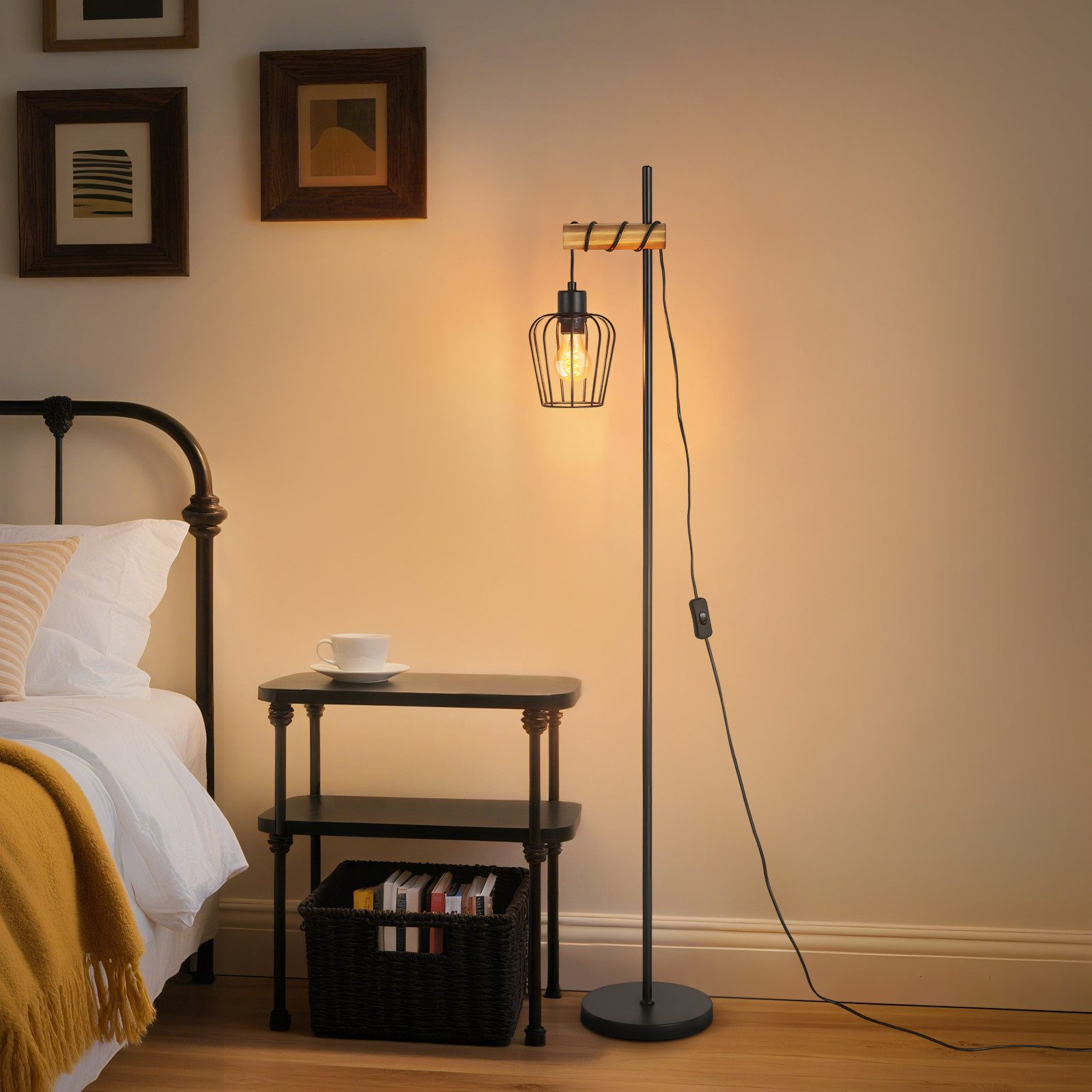 Scena di camera da letto con lampada, letto, comodino e arte incorniciata. La lampada ha un paralume a gabbia. Letto con coperta gialla.