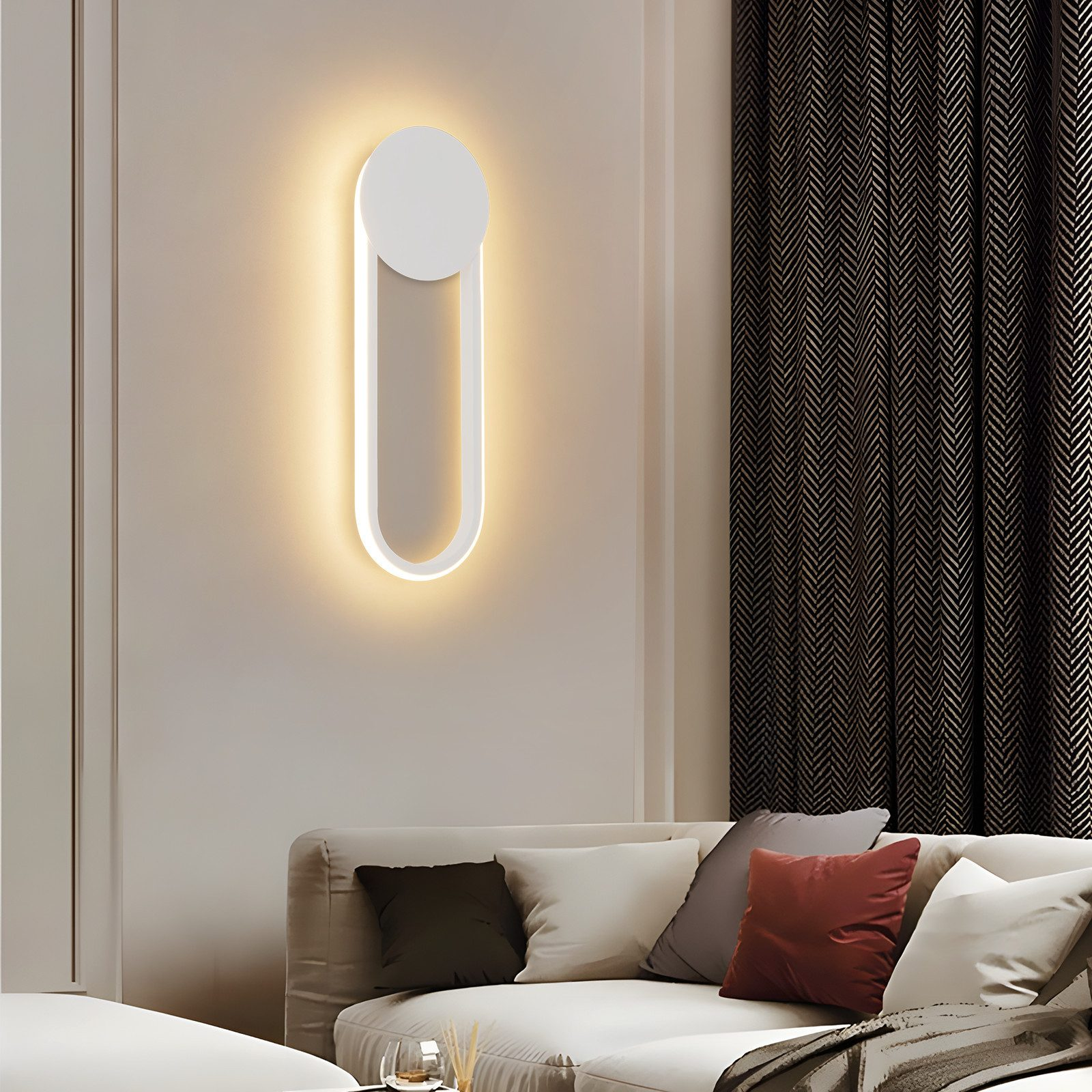 Una moderna lampada da parete dalla forma ovale luminosa. Sullo sfondo un divano con cuscini e una tenda a fantasia.