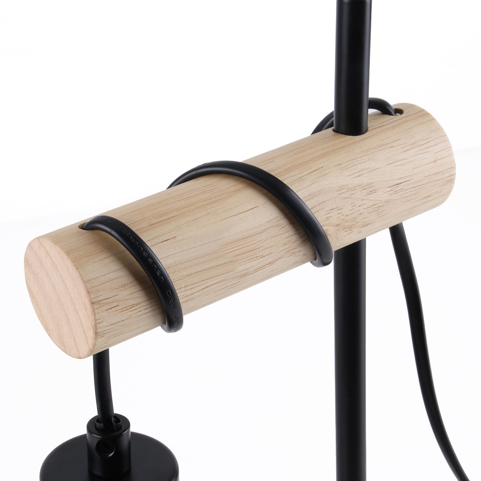 Un primo piano di una lampada. Ha un cilindro di legno e parti in metallo nero. Lo sfondo è bianco.