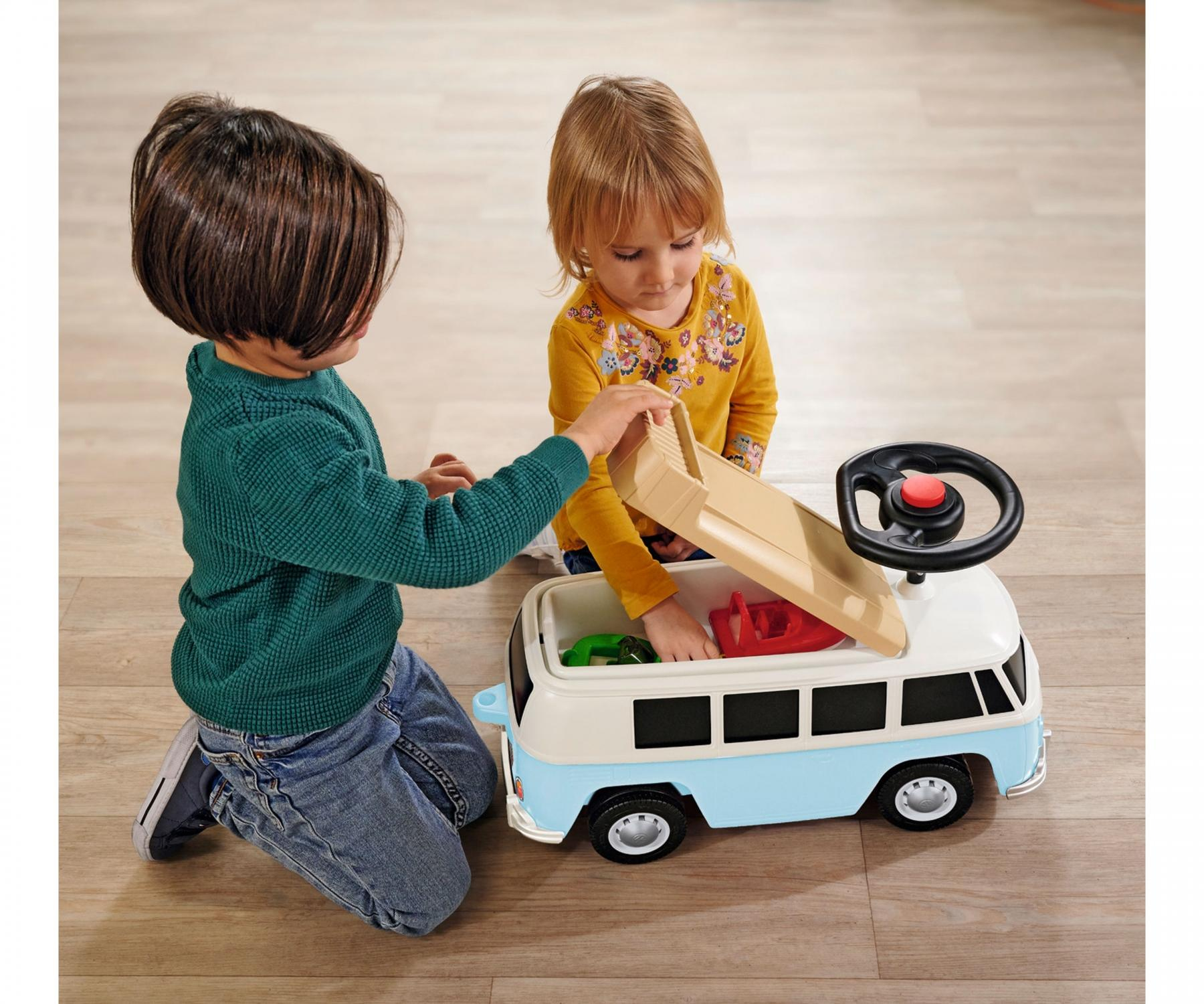 Zwei Kinder spielen mit einem blau-weißen Spielzeugbus. Ein Kind öffnet den Deckel, das andere schaut hinein.