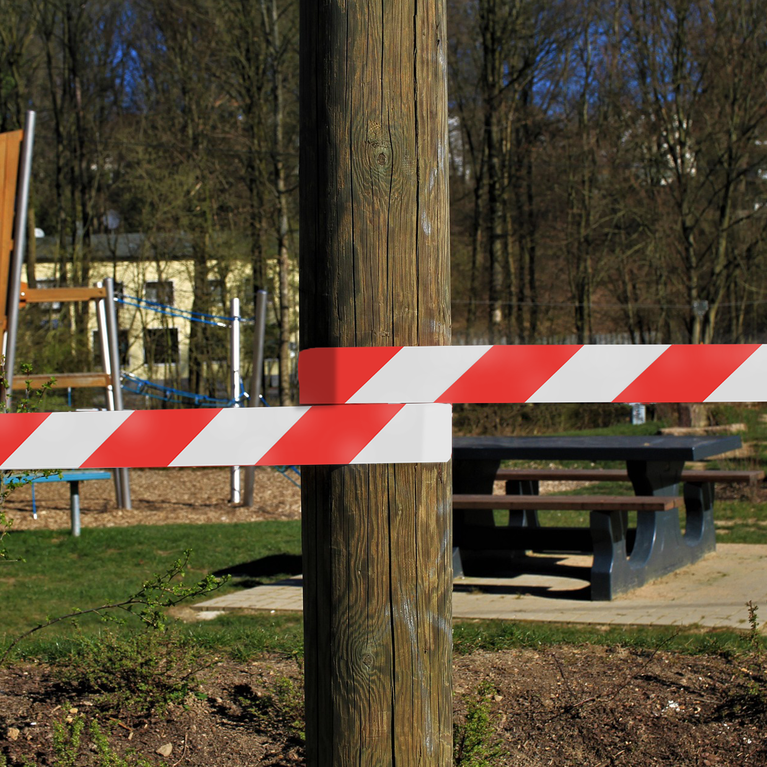 Een houten paal met rood-witte streepjes tape. Op de achtergrond zijn een speeltuin en een picknicktafel te zien.