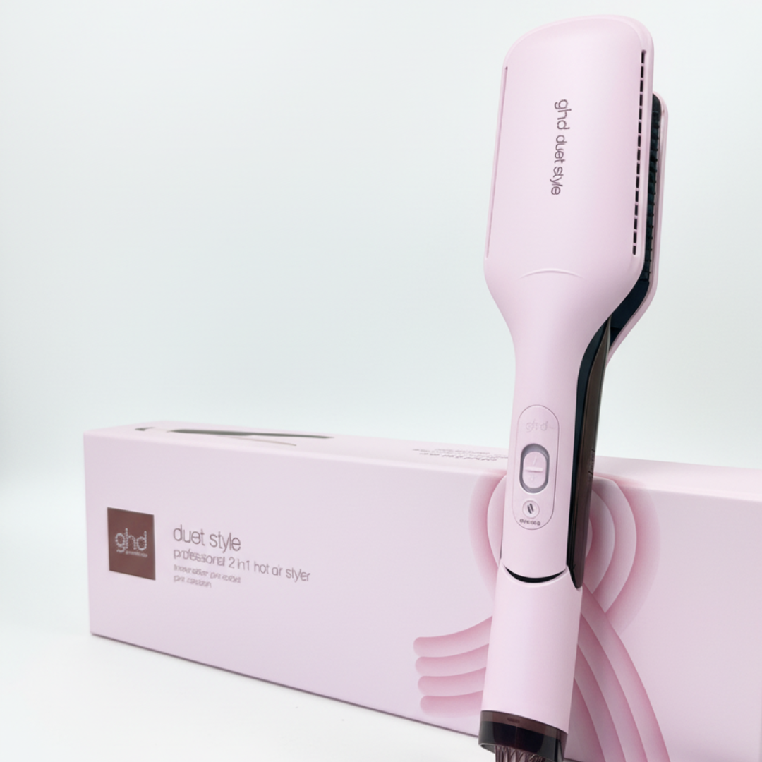 Ein pinkfarbener ghd Duett-Haarstyler und seine pinkfarbene Box stehen auf weißem Hintergrund. Der Styler steht aufrecht vor der Box.