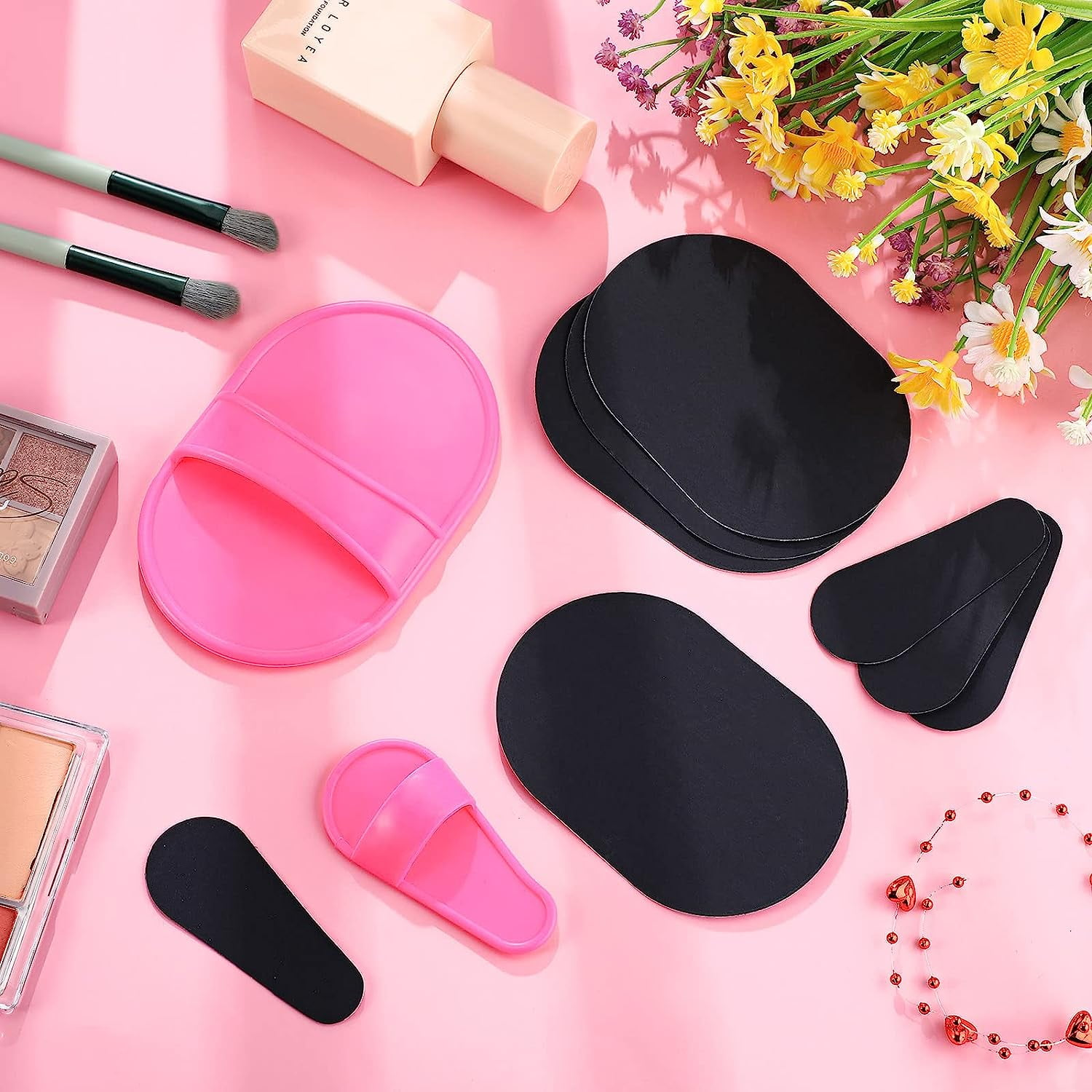 Rosa Hintergrund mit Make-up-Tools und Blumen. Enthält Pinsel, Schwämme, schwarze Pads und eine Foundation-Flasche.