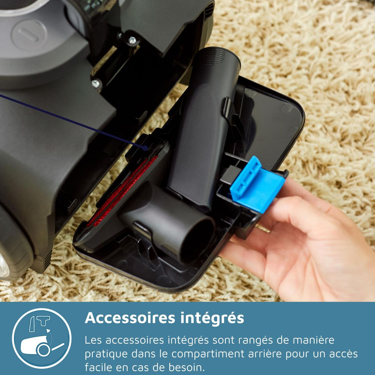 Zbliżenie odkurzacza z zintegrowanymi akcesoriami. Ręka trzyma niebieską część. Tło to beżowy dywan.