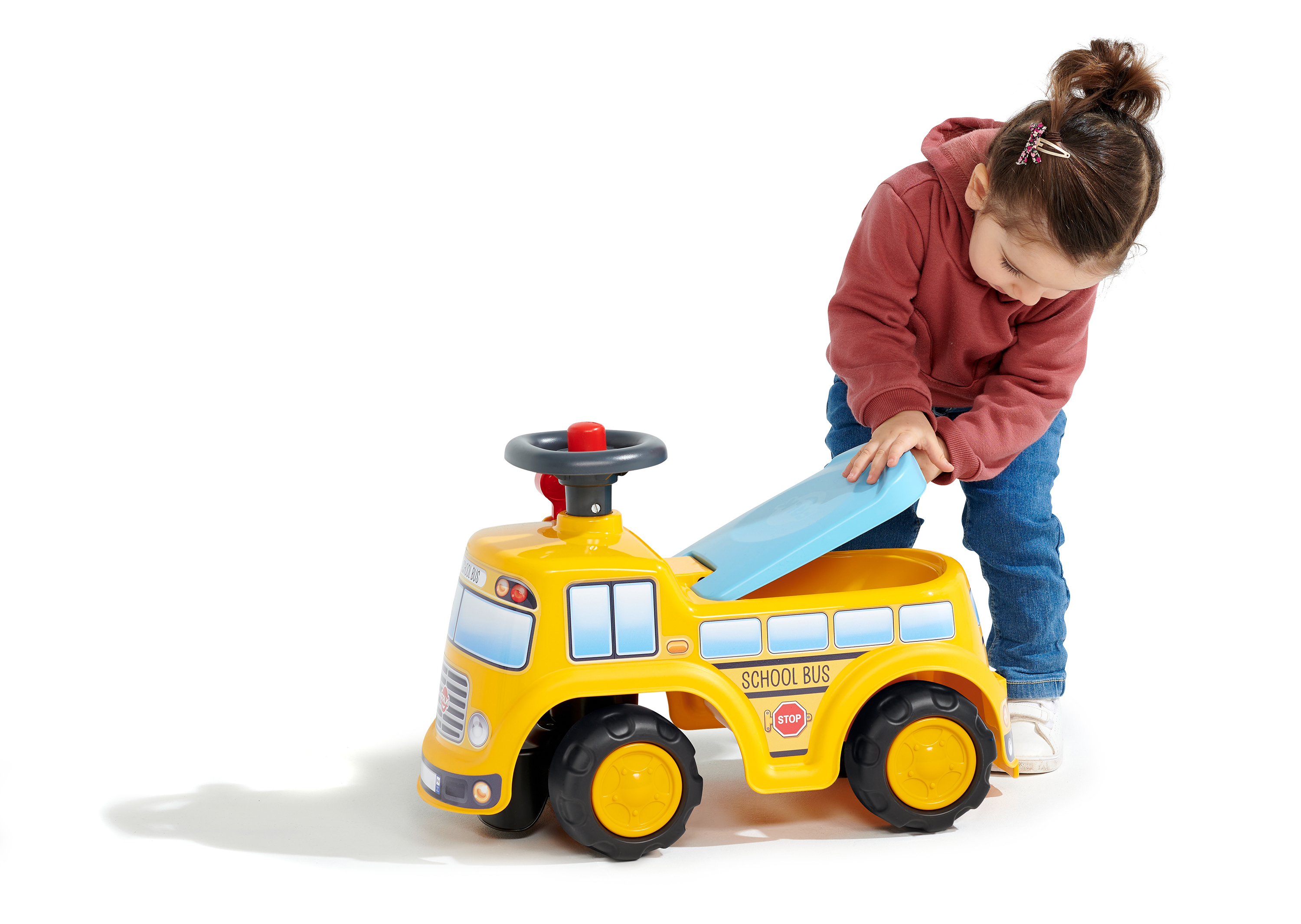 Ein Mädchen in einem roten Kapuzenpullover und Jeans spielt mit einem gelben Schulbusspielzeug.