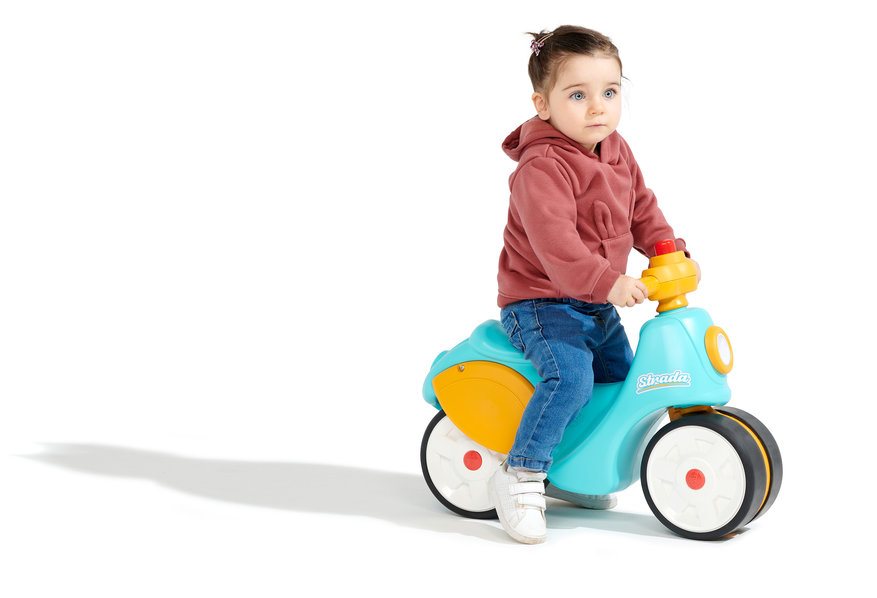 Ein Kind in einem roten Kapuzenpullover und Jeans sitzt auf einem blau-gelben Spielzeugmotorrad.