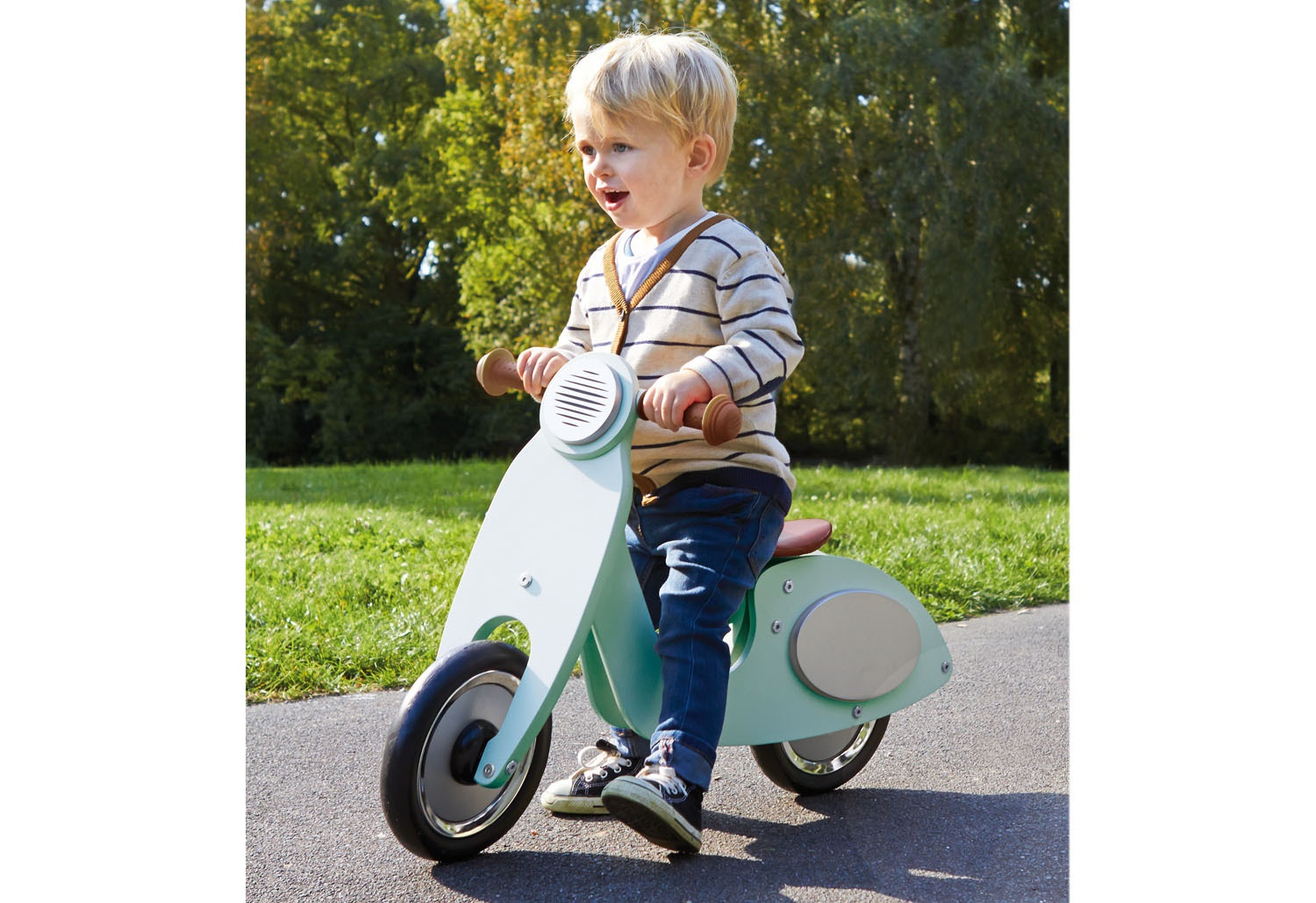 Un ragazzino guida uno scooter azzurro su un sentiero. Indossa una camicia a righe e jeans. Erba verde e alberi sullo sfondo.