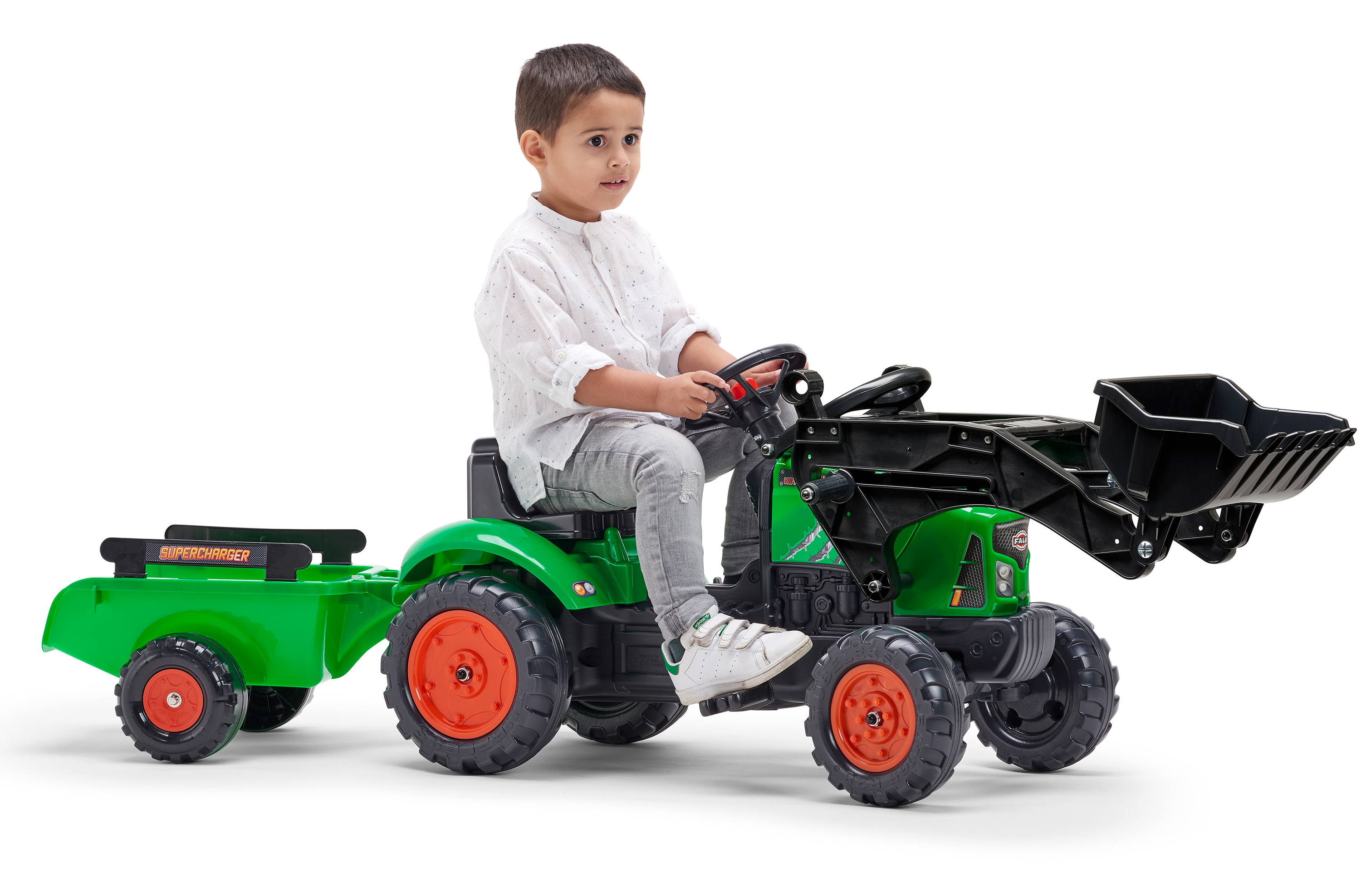 Ein Kind fährt einen grünen Traktor mit schwarzem Eimer und Anhänger auf weißem Hintergrund.