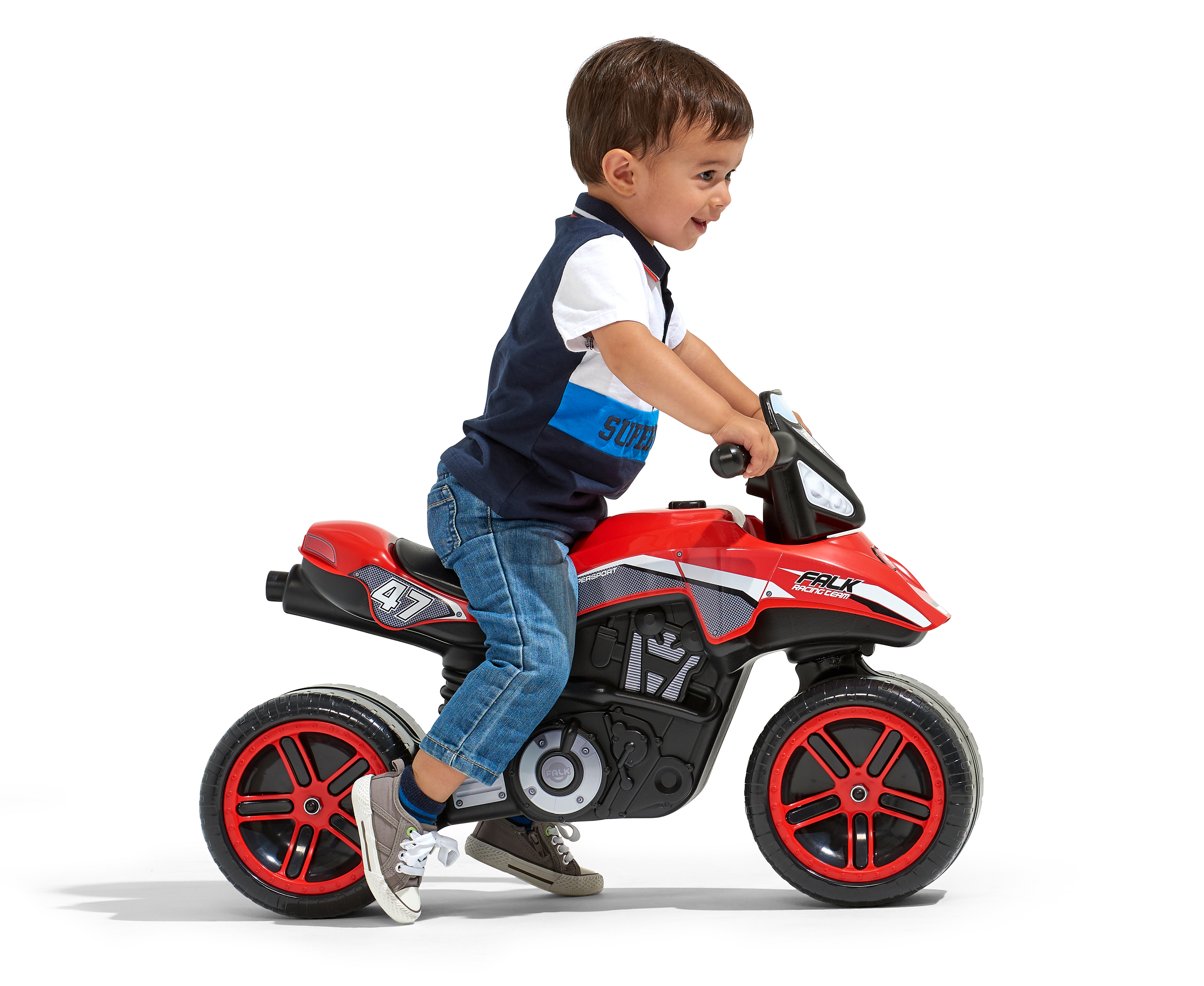Ein Kleinkind fährt ein rotes Spielzeugmotorrad. Er trägt Jeans und ein blau-weißes Hemd. Weißer Hintergrund.