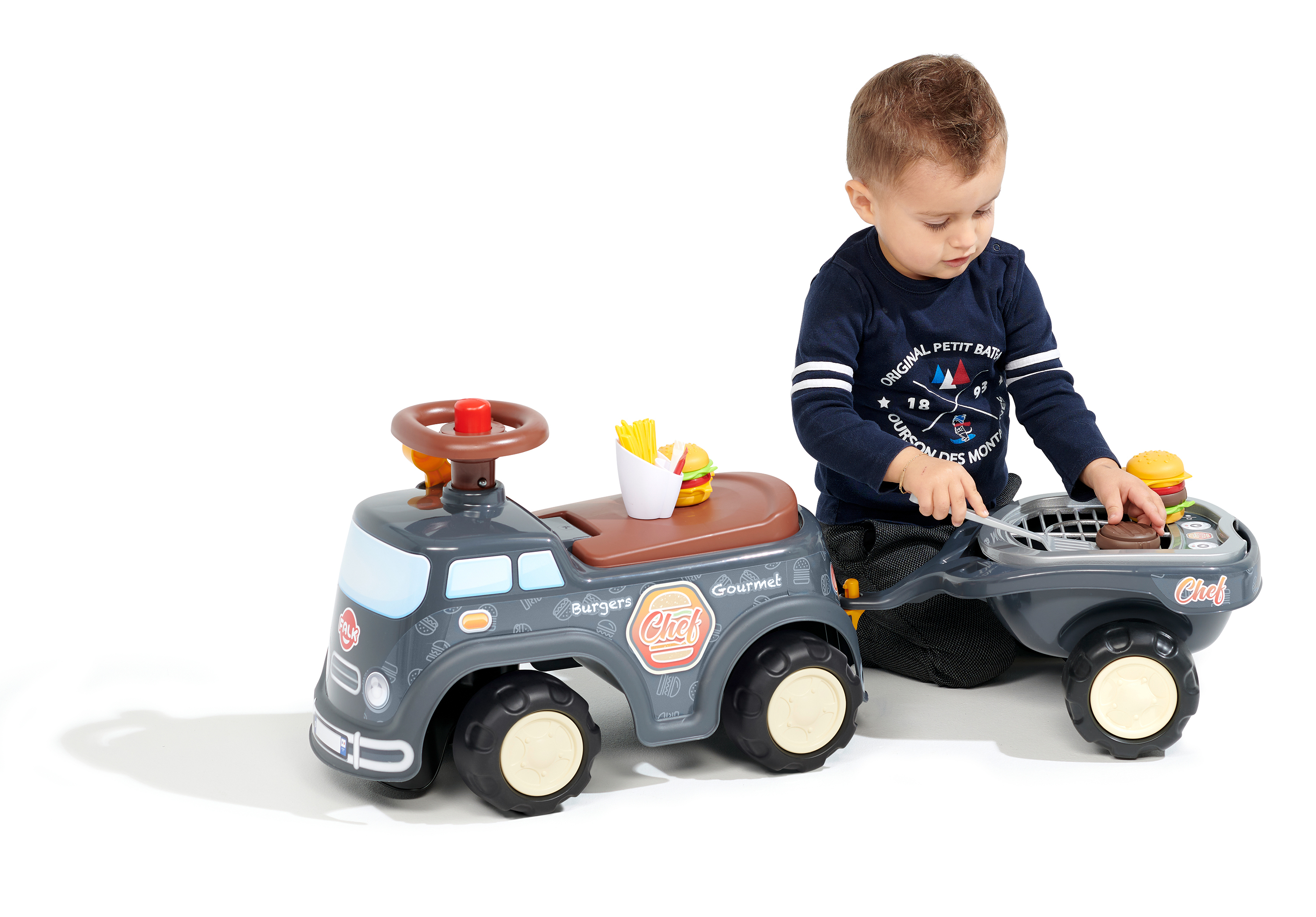 Ein Kind spielt mit einem Spielzeug-Chef-Truck. Der Truck hat einen Grill und Burger-Zubehör. Das Kind trägt ein blaues Hemd.