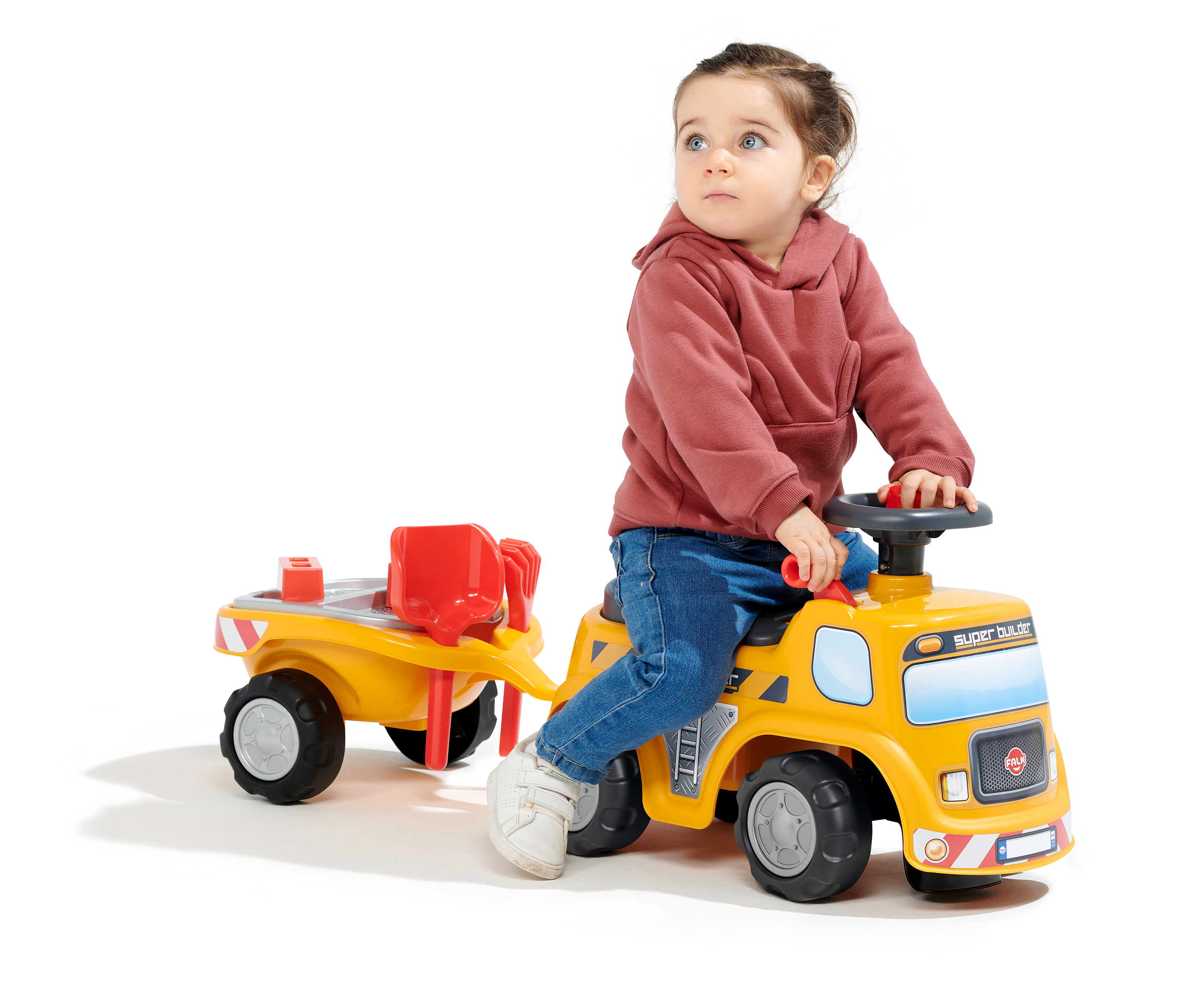 Un bambino seduto su un camion giocattolo giallo con rimorchio, con una felpa con cappuccio bordeaux e jeans, guarda in alto.
