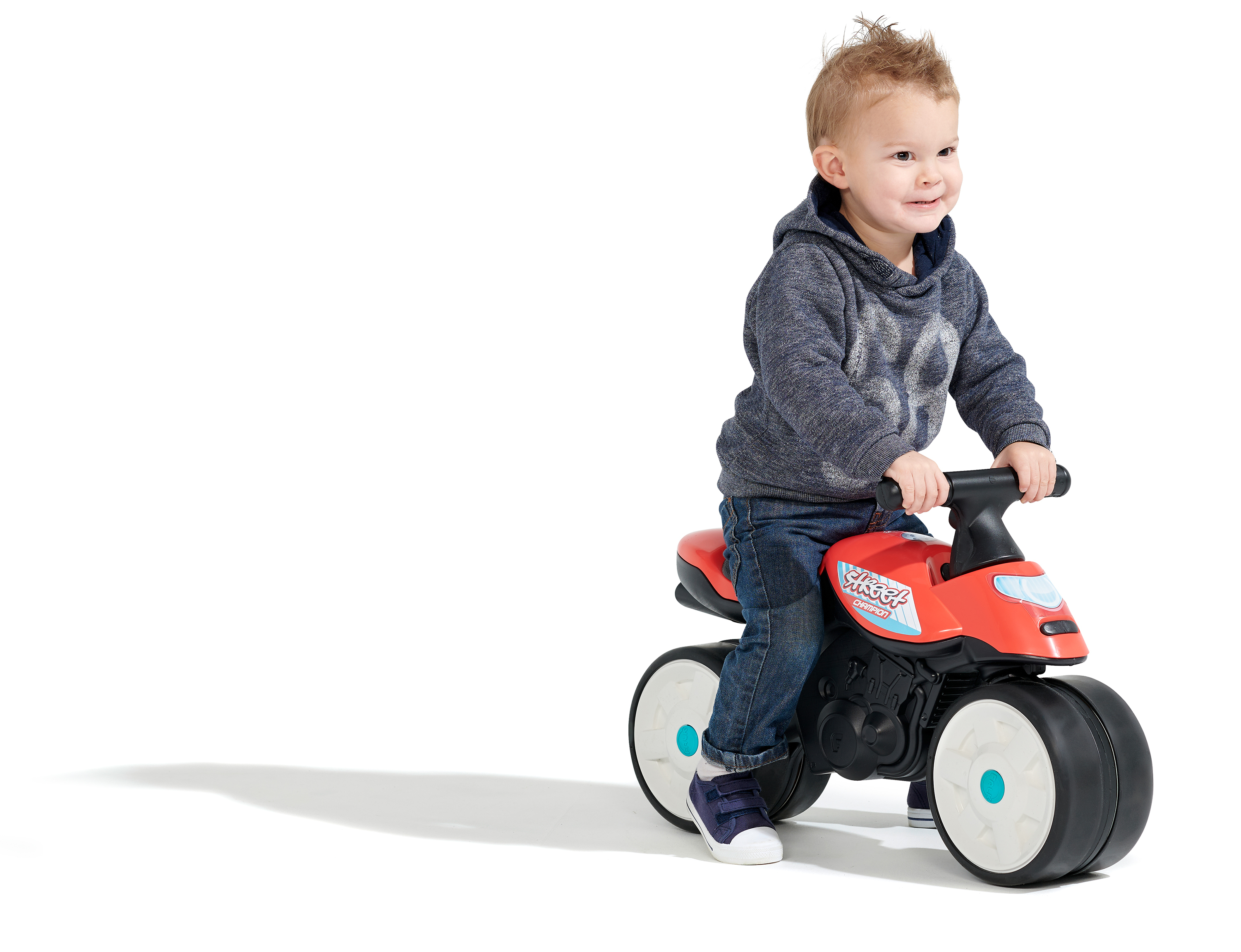 Ein Kleinkind sitzt lächelnd auf einem roten Spielzeugmotorrad. Der Hintergrund ist weiß.