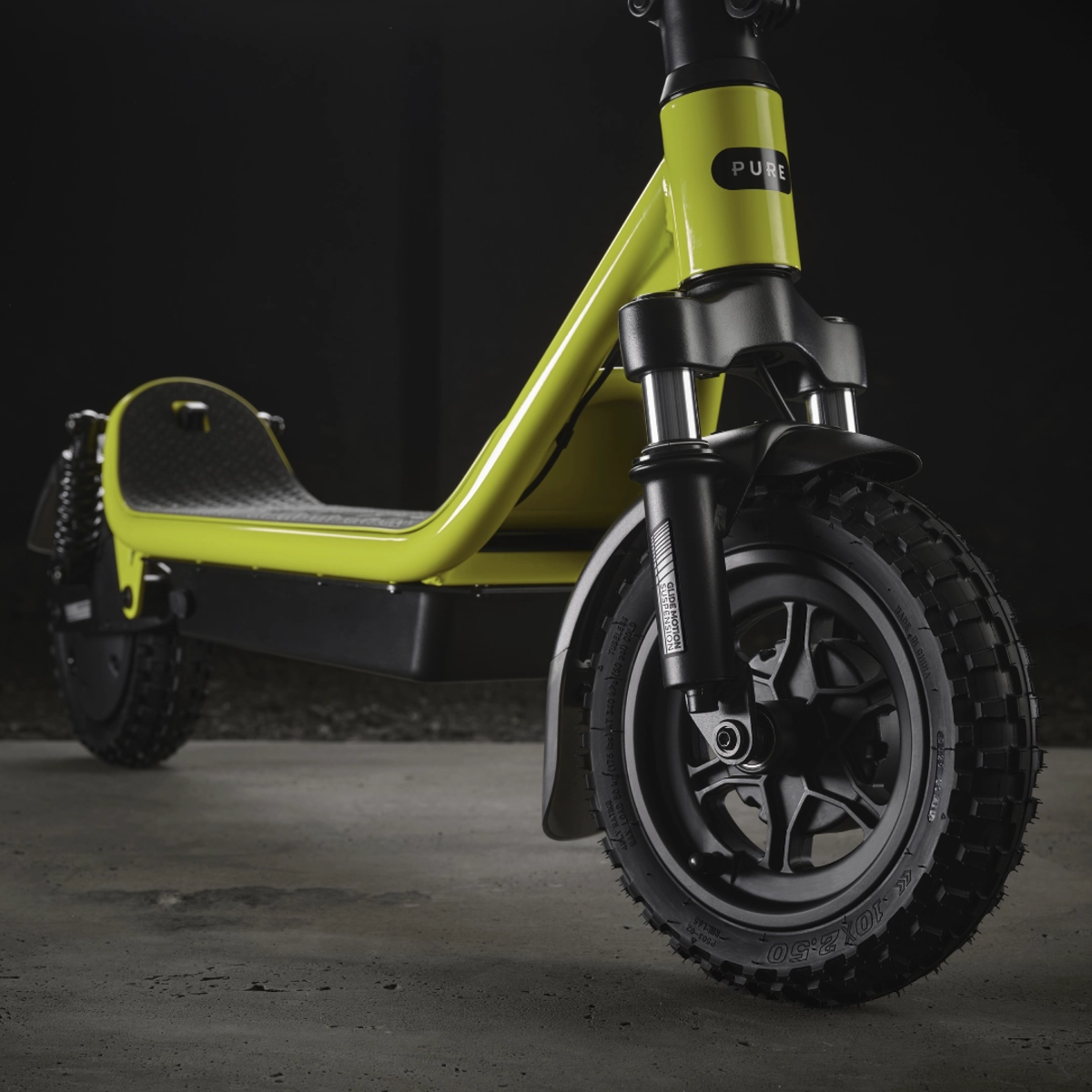 Ein limettengrüner Elektroroller mit schwarzen Reifen und Akzenten. Der Roller steht auf einer Betonoberfläche vor schwarzem Hintergrund.