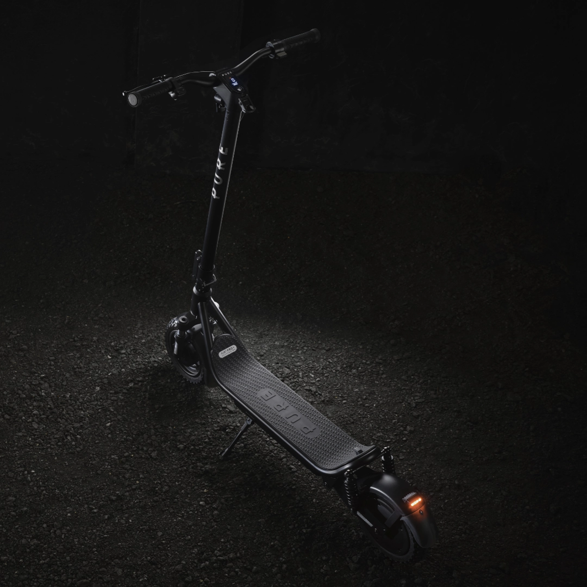 Ein schwarzer Elektroroller mit dem Namen PURE auf dem Deck steht auf dunklem Asphalt. Der Roller hat ein Licht hinten.