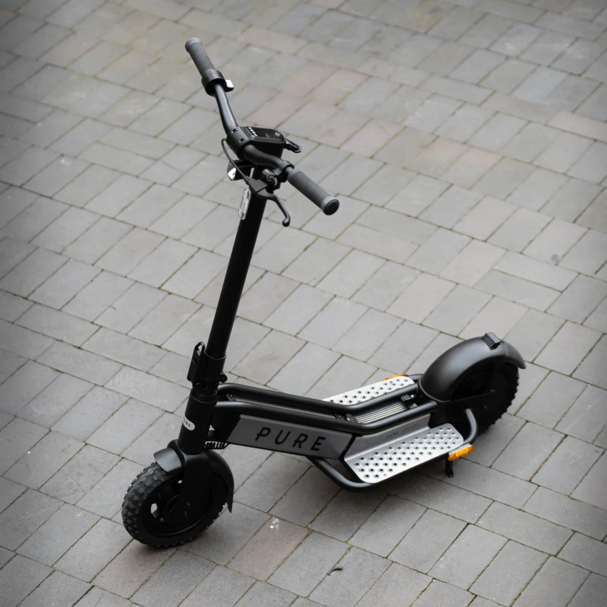 Schwarzer Elektroroller auf grauem Ziegeluntergrund. Der Roller hat einen schwarzen Rahmen, Räder und Lenker. Er ist mit 'PURE' beschriftet.