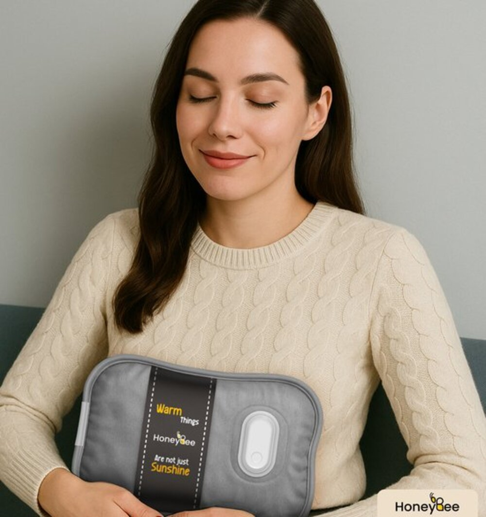 A woman with eyes closed holds a gray heating pad. The pad has text: Warm Things, HoneyBee, Are not just Sunshine. She wears a cream sweater.
