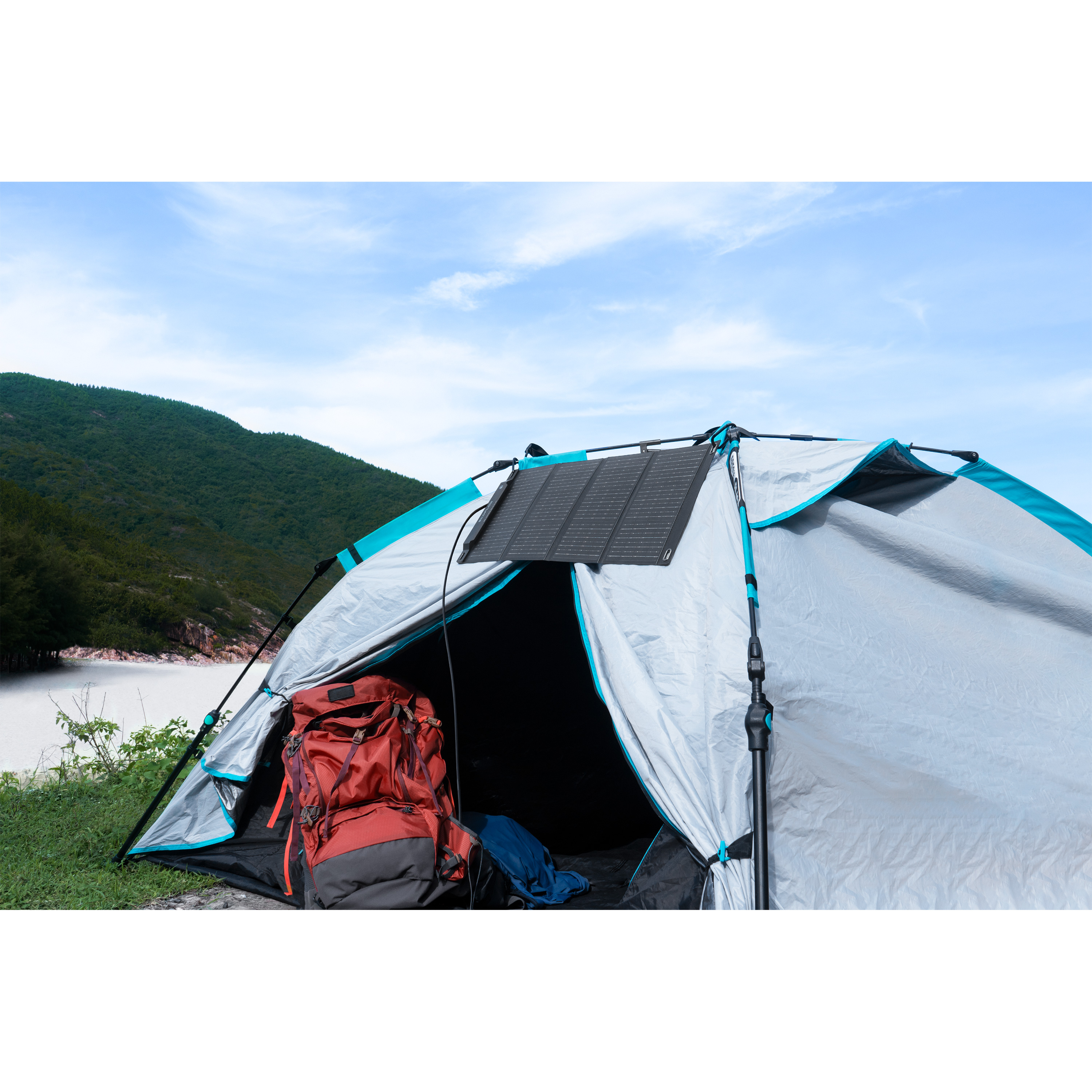 Una tienda de campaña con panel solar, mochila roja dentro. Montañas verdes y cielo azul al fondo.