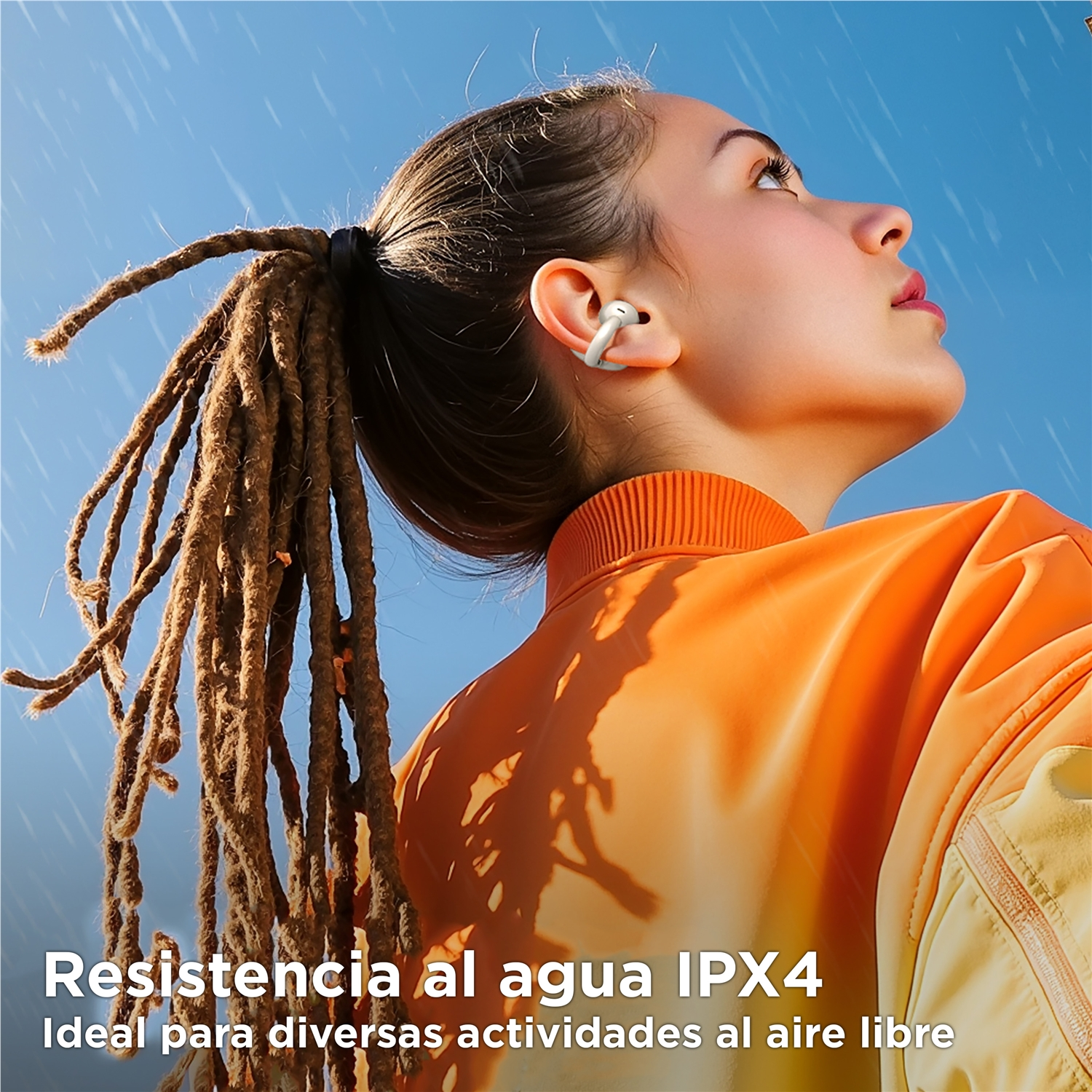 Una donna con i dreadlock indossa auricolari, guardando in alto. Ha una giacca arancione, cielo blu e testo sulla resistenza all'acqua.
