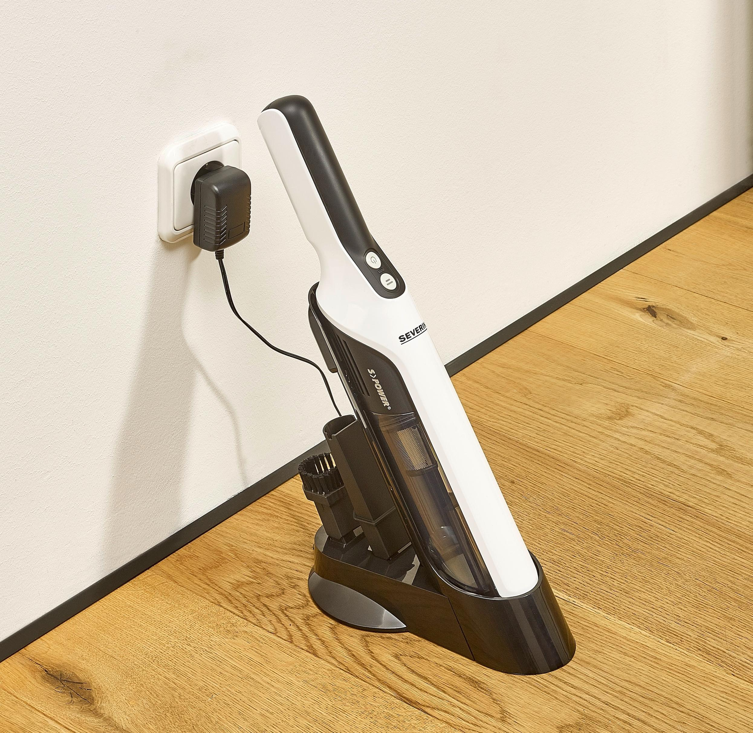 Biało-czarny odkurzacz bezprzewodowy w stacji ładującej, podłączony do gniazdka ściennego, na drewnianej podłodze.