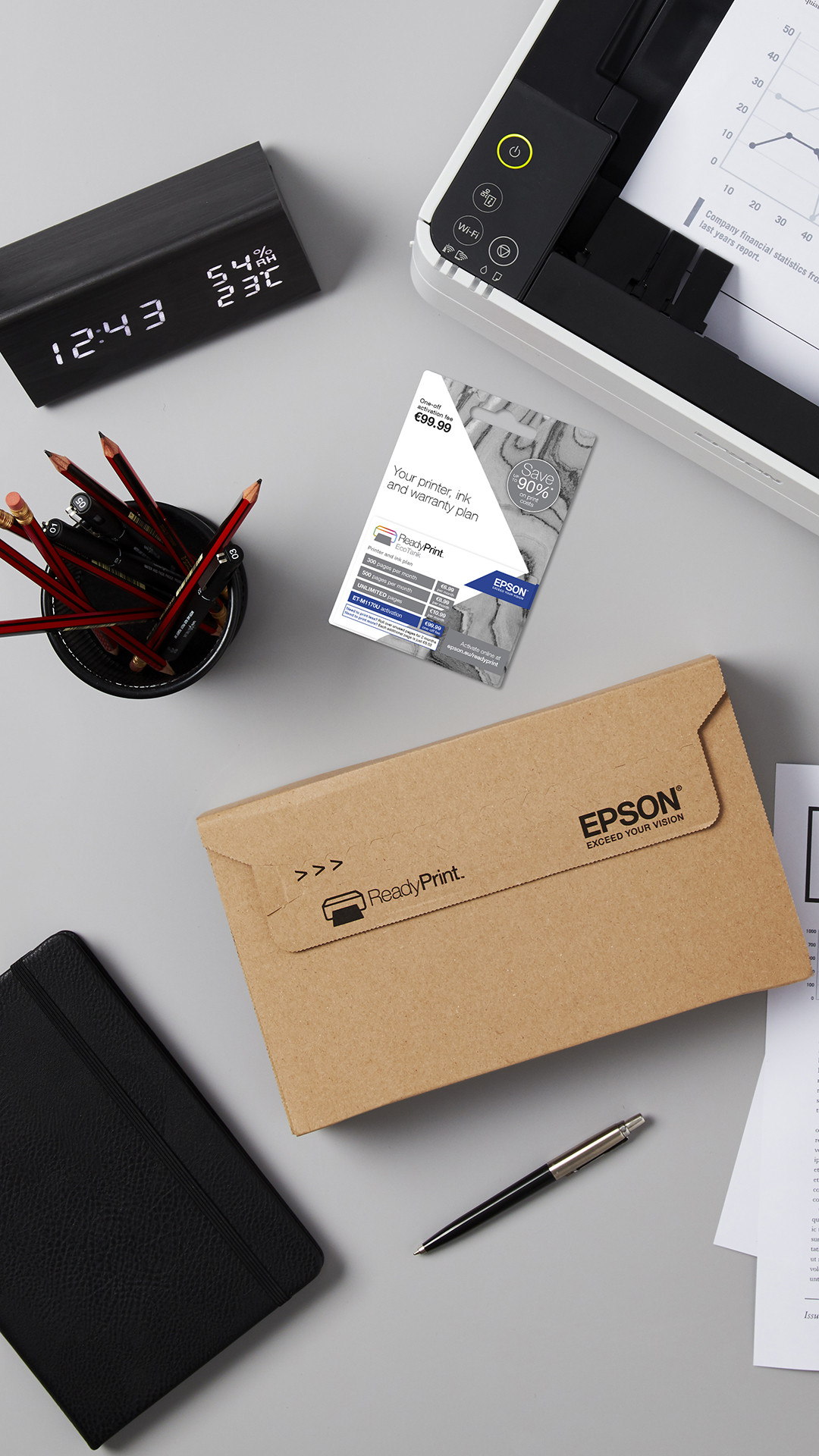 Scena biurowa z drukarką, zegarem, ołówkami, długopisem, notatnikiem i kopertą ReadyPrint, wraz z papierami i planem tuszu Epson.