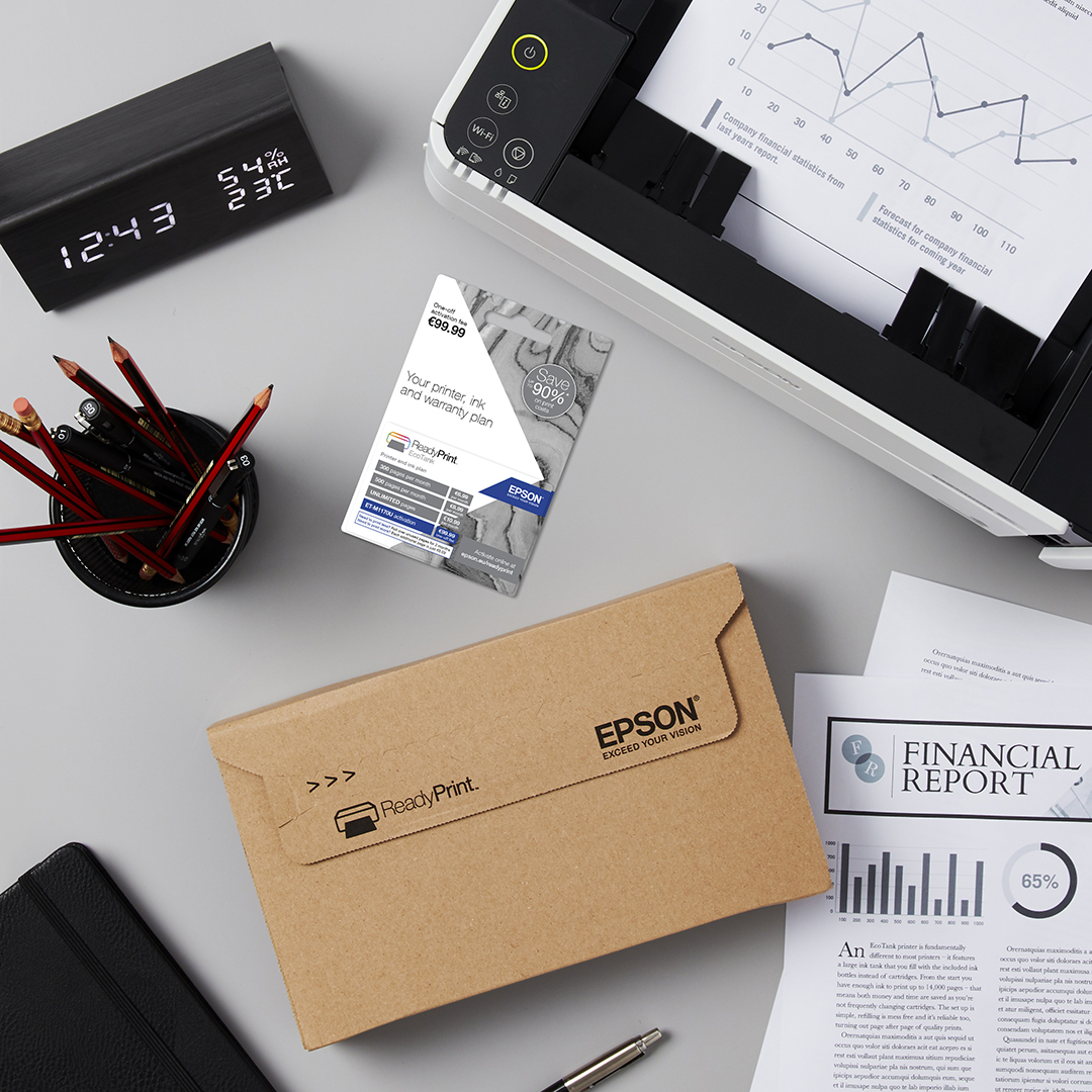 Scena na biurku: Drukarka, zegar, ołówki, koperta Epson, raport finansowy, opakowanie z tuszem i dokumenty.