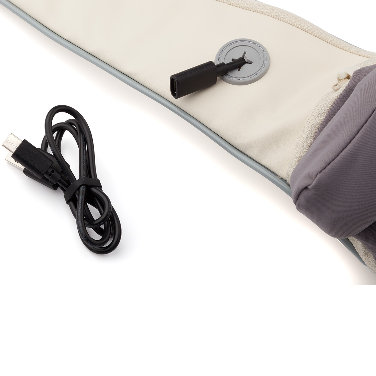 Un dispositivo crema con borde gris y cable negro sobre fondo blanco. Se ve un botón circular y una cremallera.