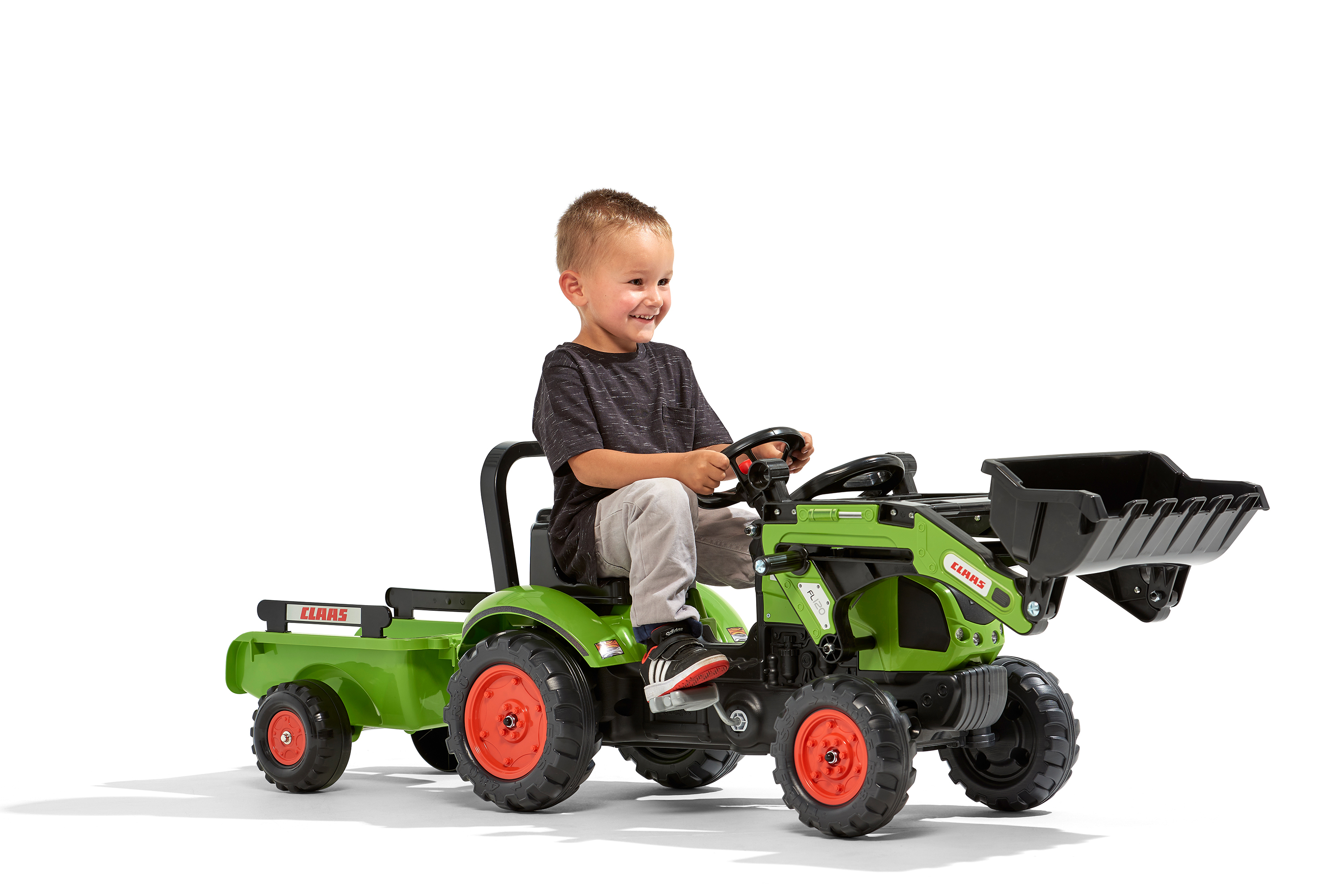 Ein lächelnder Junge fährt einen grünen Spielzeugtraktor mit Anhänger. Der Traktor hat orangefarbene Räder.
