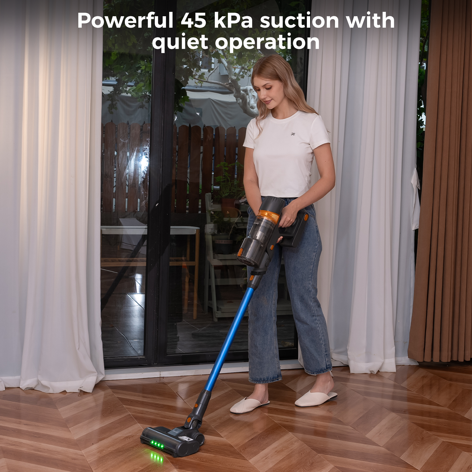 Une femme utilise un aspirateur sans fil sur un sol en bois. Elle porte une chemise blanche et un jean.