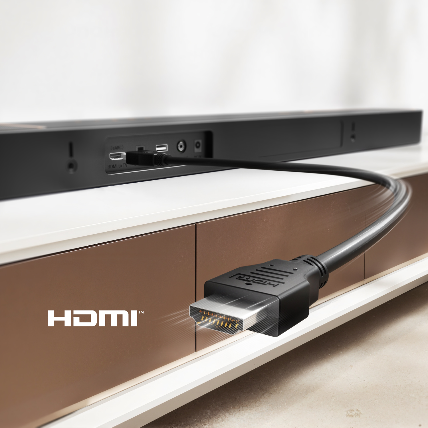 Kabel HDMI podłączony do soundbaru. Soundbar znajduje się na białej i brązowej szafce. Widoczne logo HDMI.