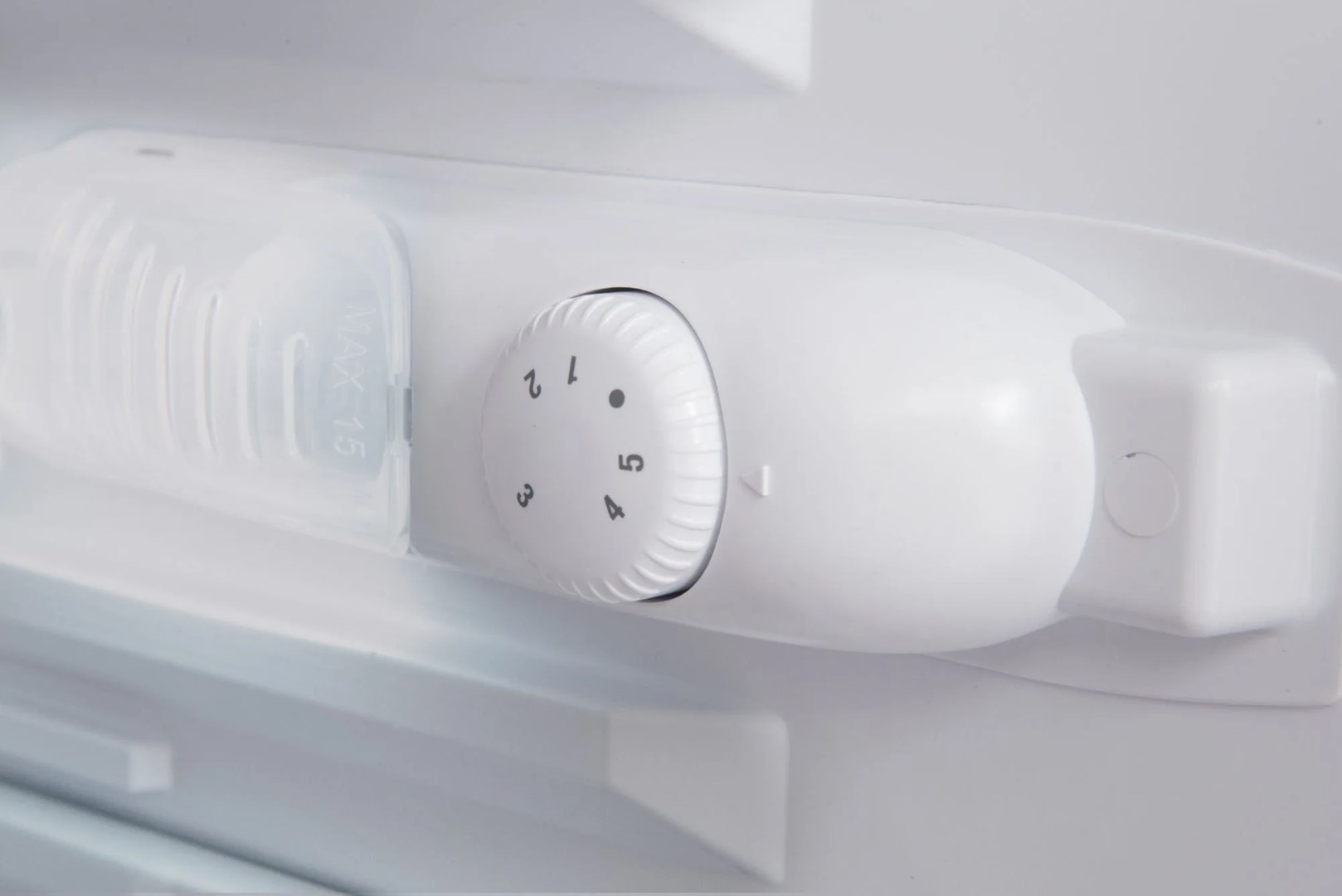 Zbliżenie białego elementu lodówki. Pokrętło pokazuje liczby 1-5, przezroczyste plastikowe pudełko i biała konstrukcja z przyciskiem.