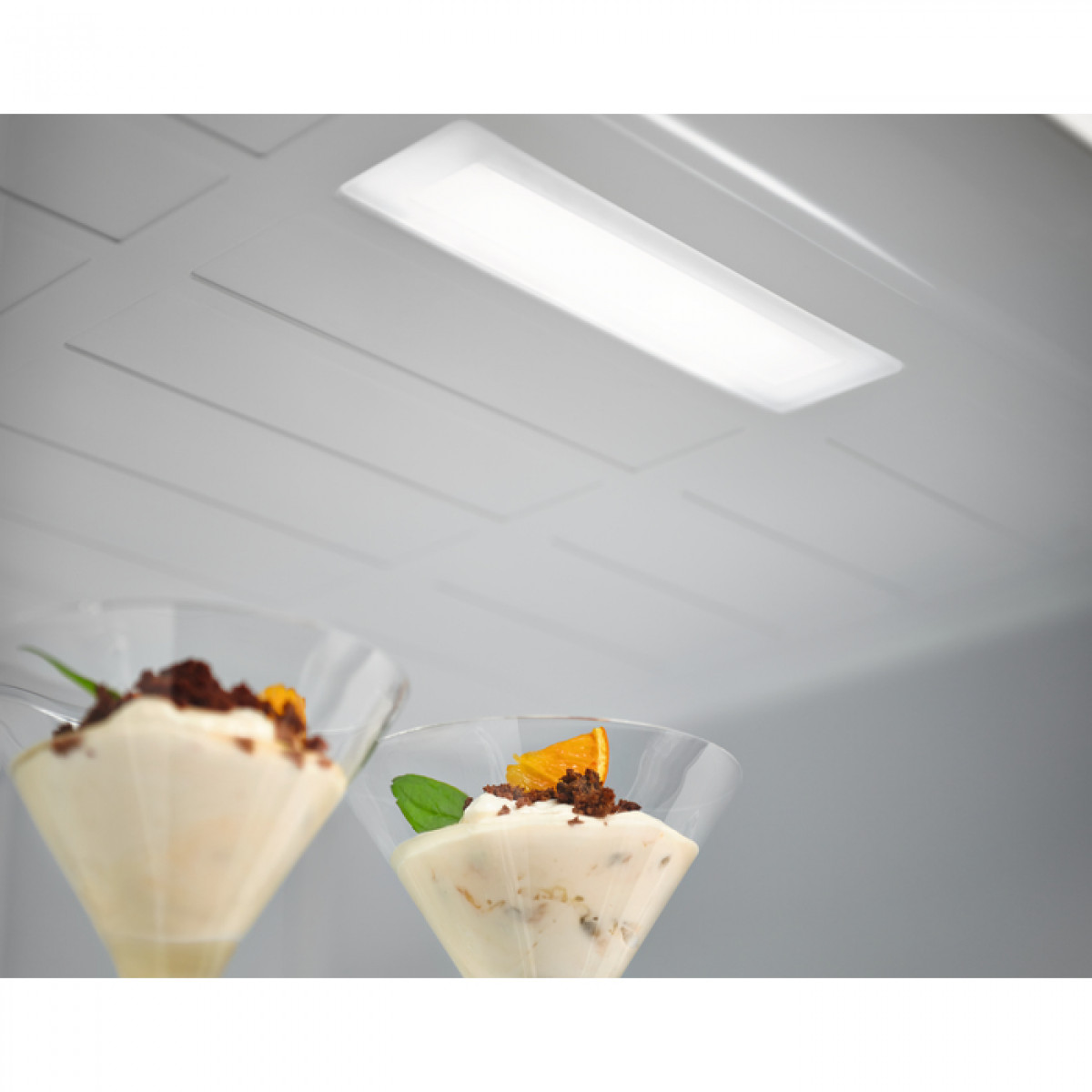 Dwa kieliszki do deserów z kremowymi deserami, plasterkami pomarańczy i wiórkami czekoladowymi pod lampą sufitową.