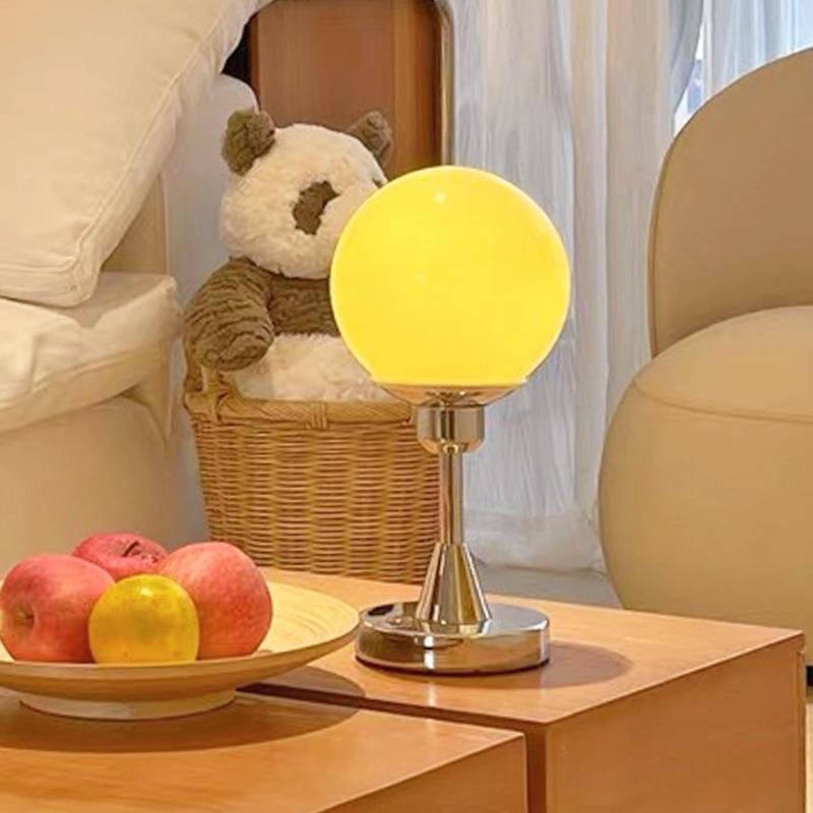 Eine gelbe Kugellampe steht auf einem Holztisch. Äpfel und ein Panda-Plüschtier befinden sich in der Nähe.