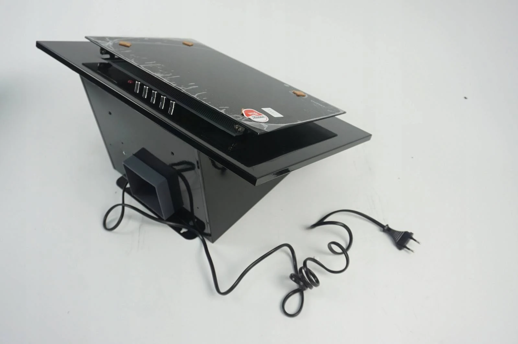 Czarny okap kuchenny na białej powierzchni. Ma szklany blat, panel sterowania i przewód zasilający.