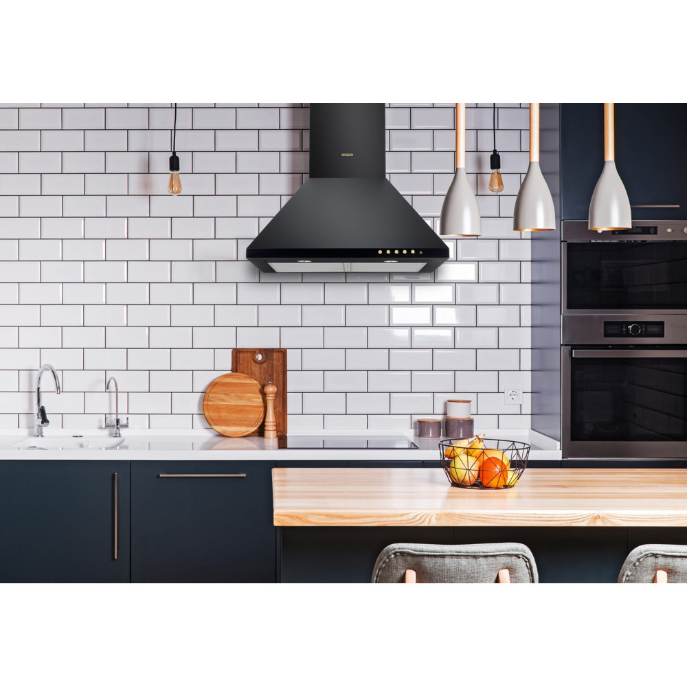 Nowoczesna kuchnia z czarnym okapem, białymi kafelkami, drewnianym blatem, koszem z owocami i ciemnoniebieskimi szafkami.