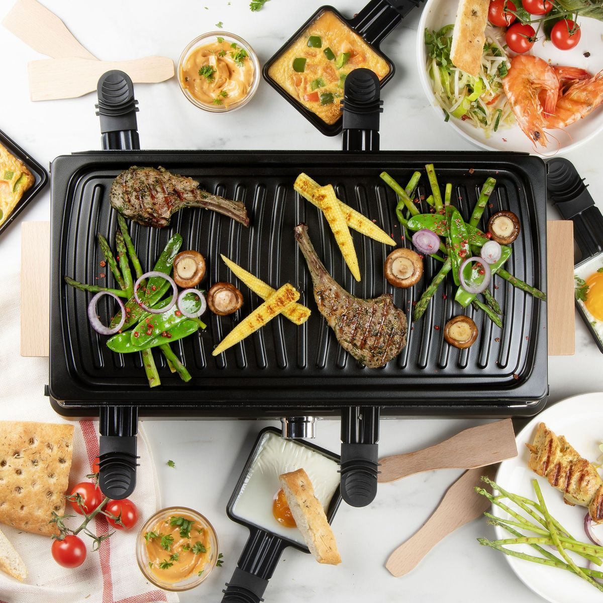 Draufsicht auf einen Grill mit Fleisch, Gemüse und anderen Gerichten. Enthält Lammkoteletts, Mais, Pilze und Saucen.