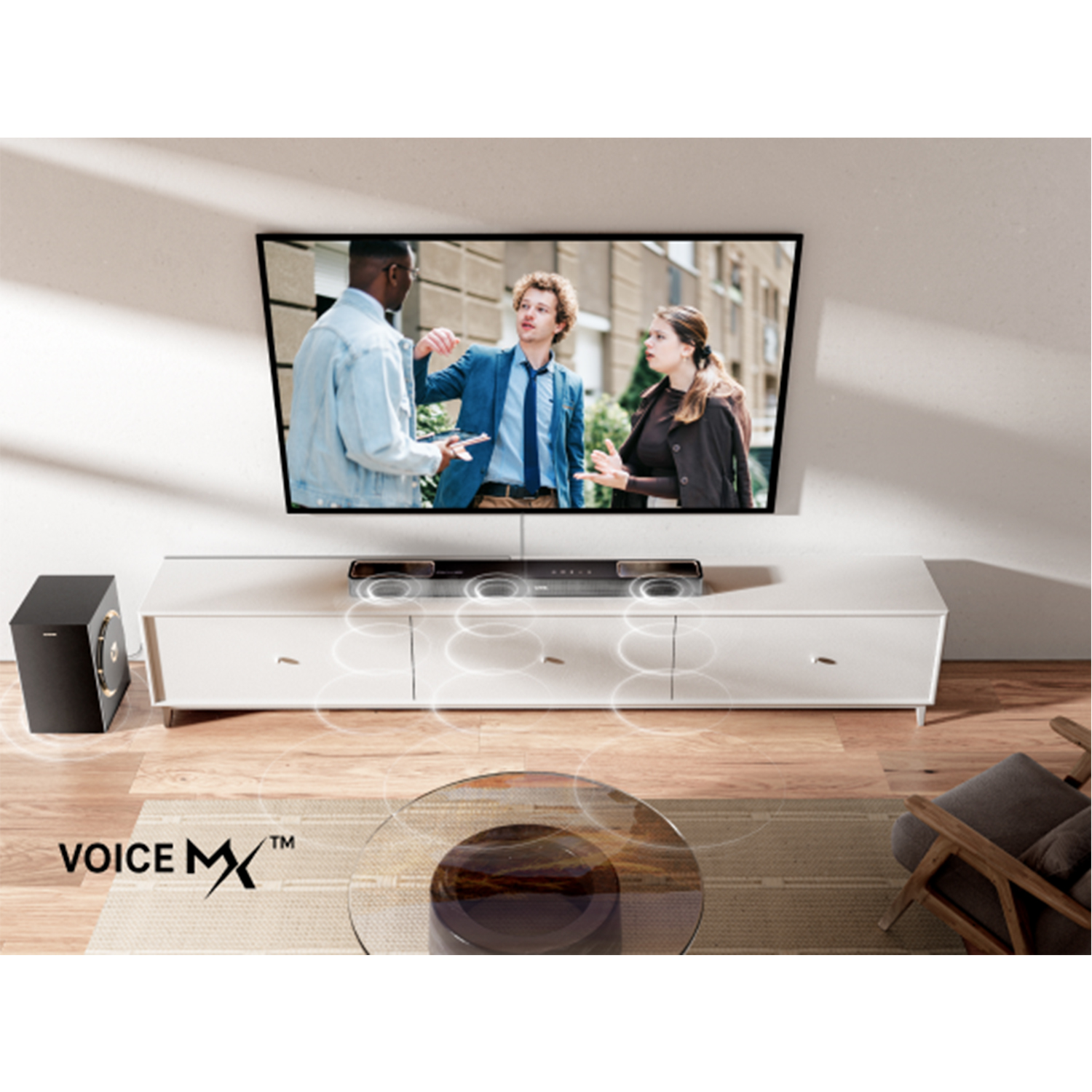Telewizor wyświetla ludzi. Poniżej biała szafka z soundbarem, subwooferem i szklanym stołem z logo Voice MX.