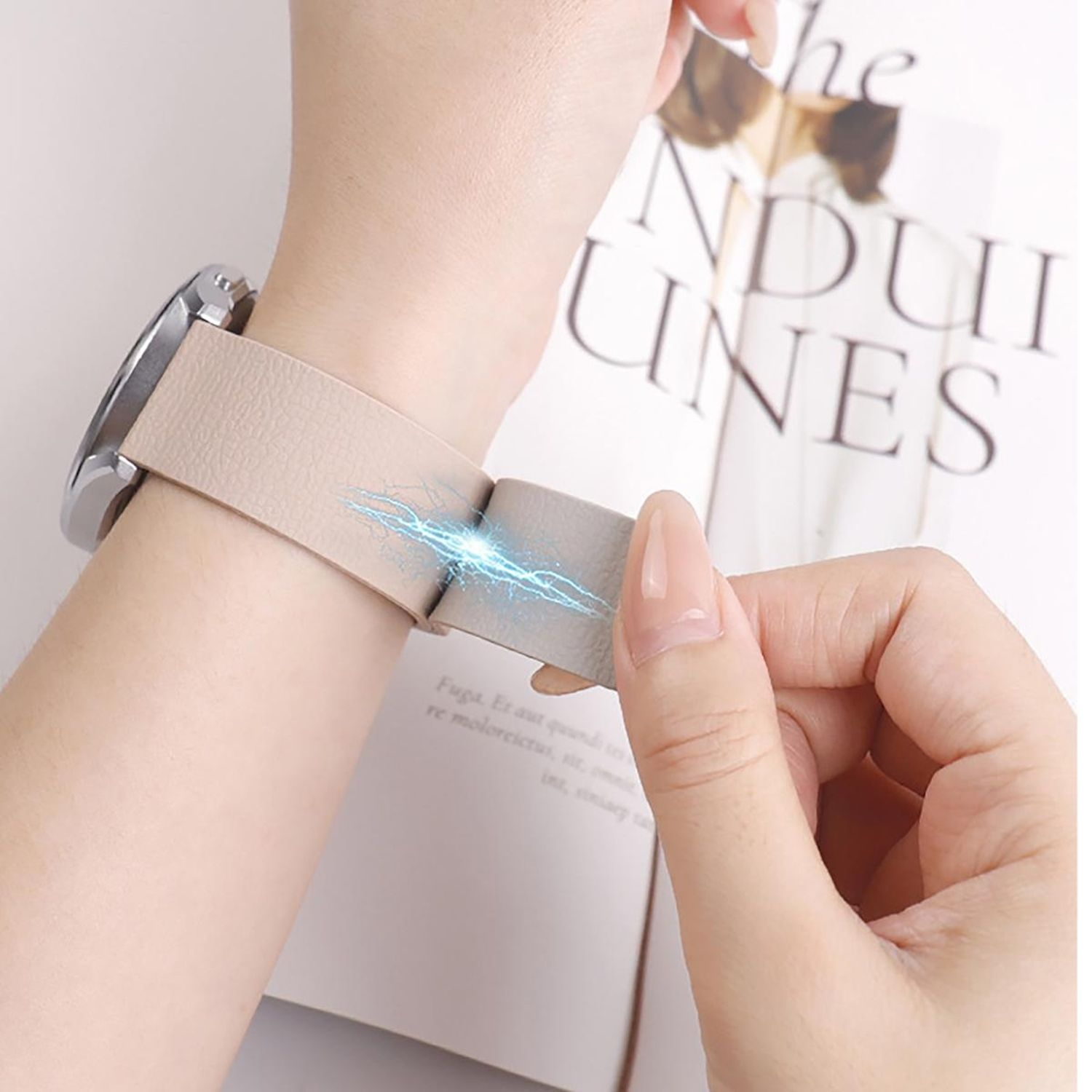 Handgelenk mit Uhr. Eine Hand hält das Uhrenarmband, mit blauen blitzartigen Grafiken darauf. Im Hintergrund ein Buch.