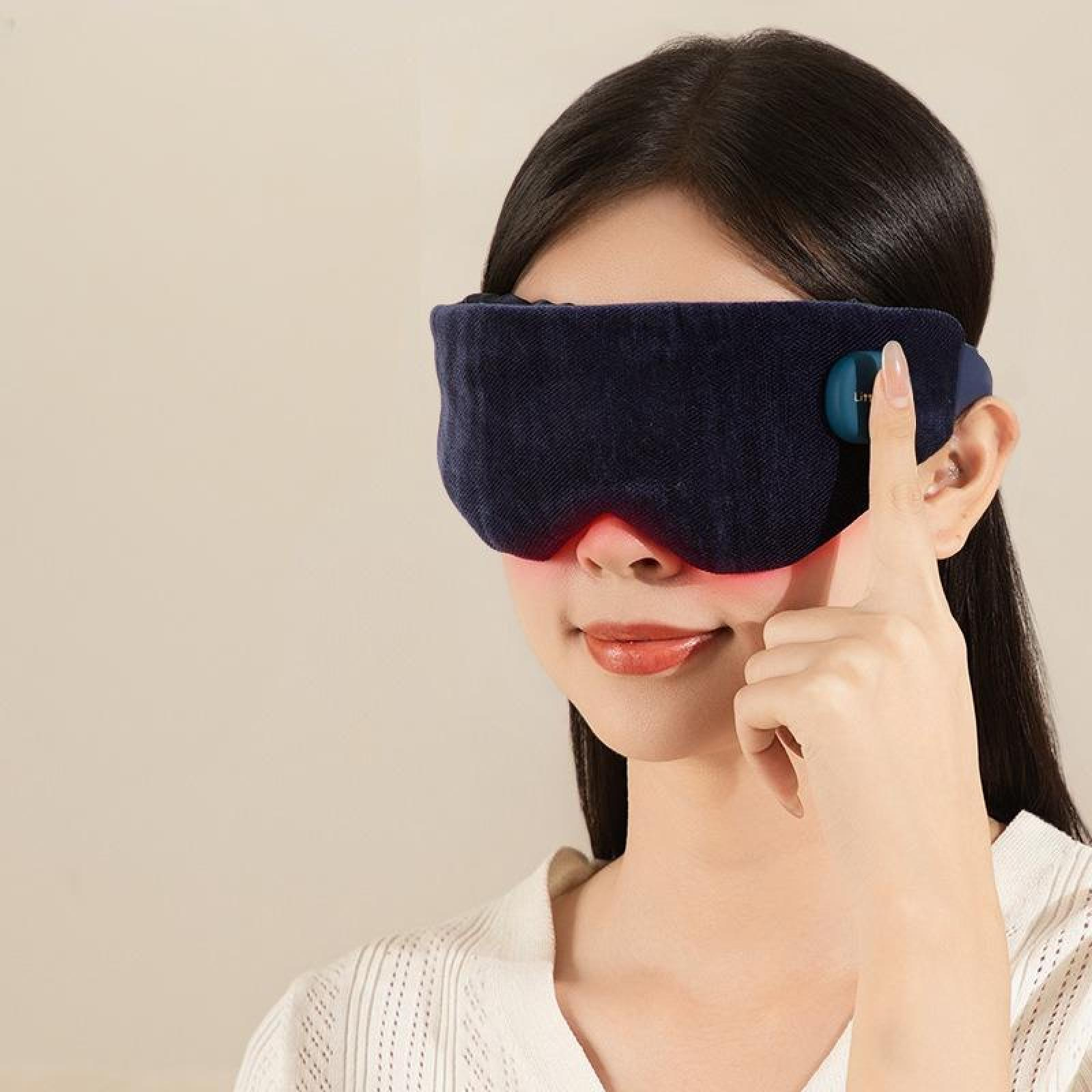 Eine Frau mit einer dunkelblauen Augenmaske mit rotem Licht. Sie zeigt mit dem Finger auf die Maske.