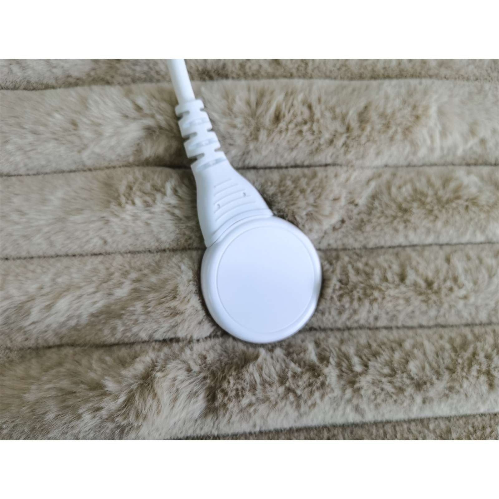 Ein weißer Stecker, der mit einem weichen, flauschigen, beigefarbenen Heizkissen verbunden ist. Das Kissen hat horizontale Rippen.