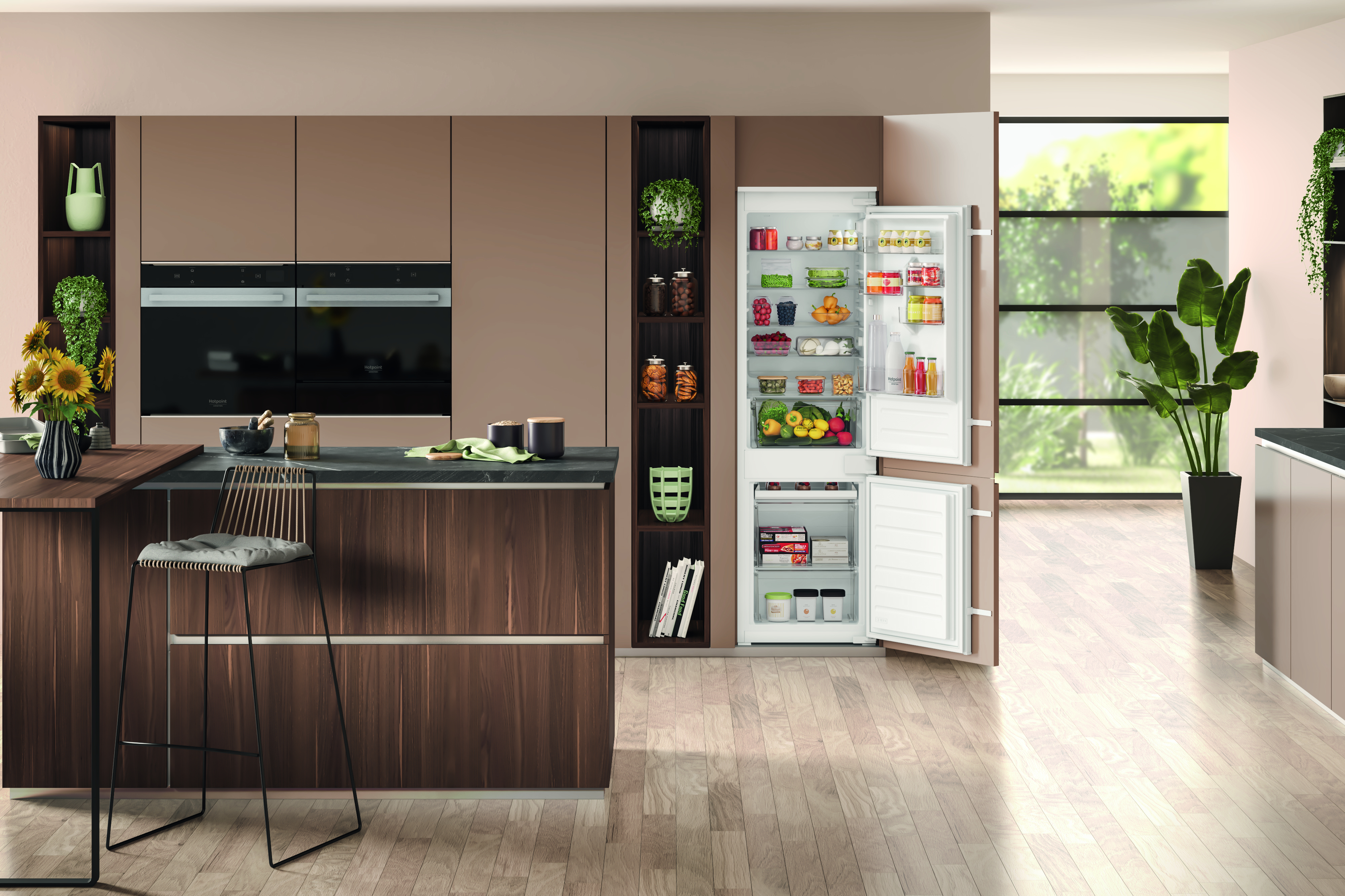 Cucina moderna con frigorifero aperto, isola e sgabello. Include forni, piante e barattoli. Pavimento in legno chiaro.