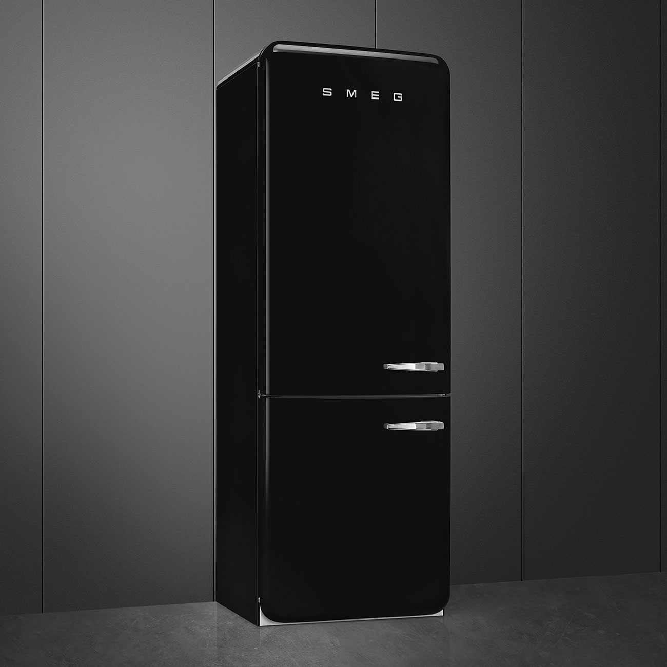 Un refrigerador SMEG negro está contra una pared gris oscuro. Tiene dos puertas con manijas plateadas. El suelo es gris.