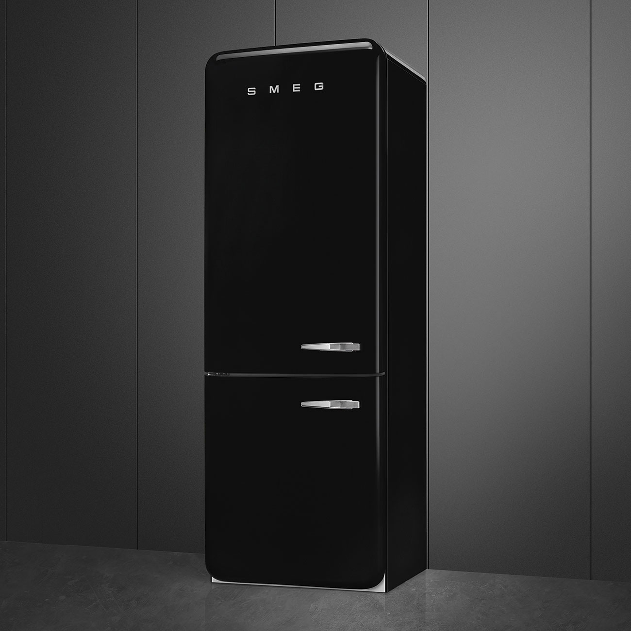 Un refrigerador SMEG negro está contra una pared gris oscuro. El refrigerador tiene dos puertas y manijas cromadas. El suelo es gris.