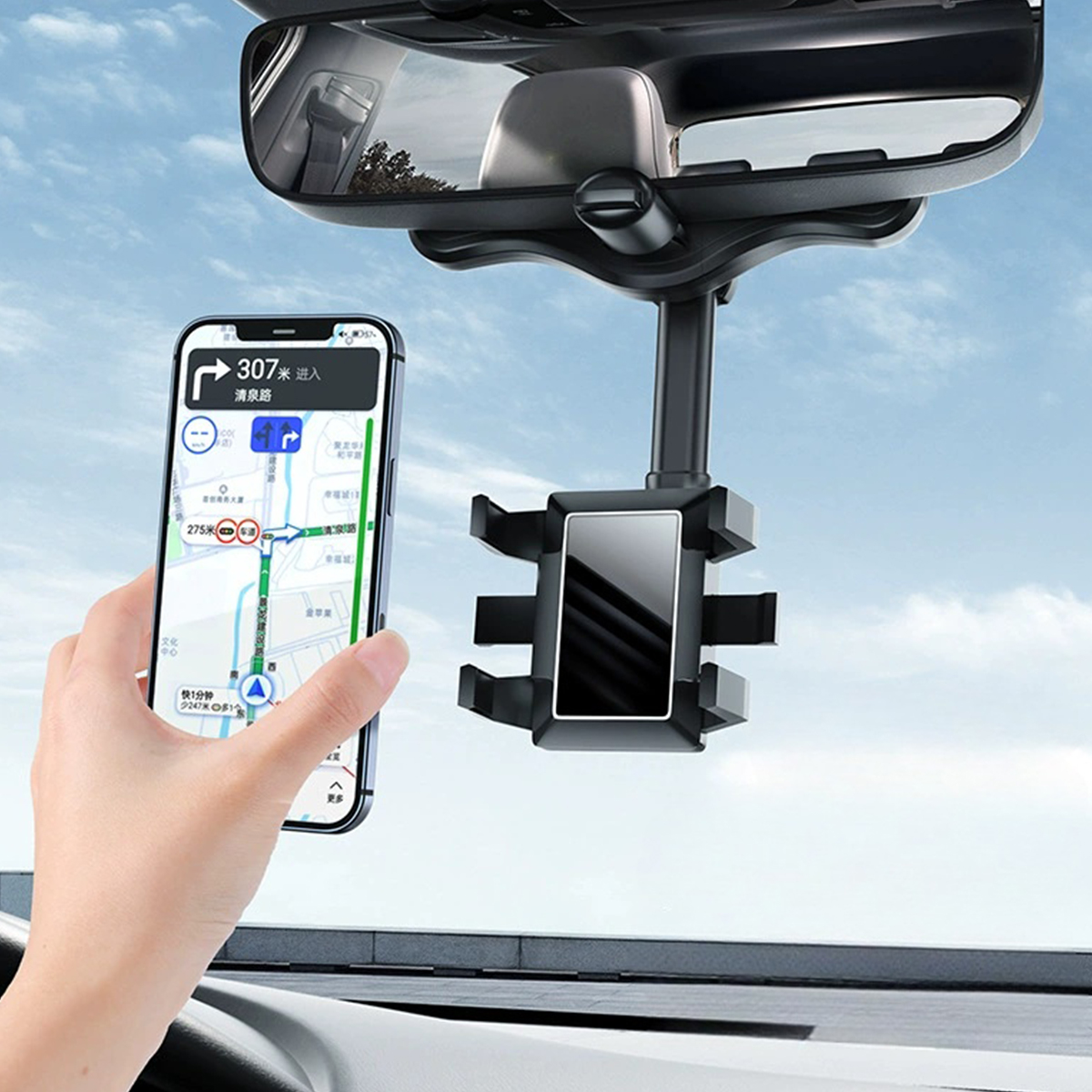 Eine Hand, die ein Telefon mit einer Navigations-App hält. Eine Autotelefonhalterung ist am Rückspiegel befestigt. Himmel im Hintergrund.